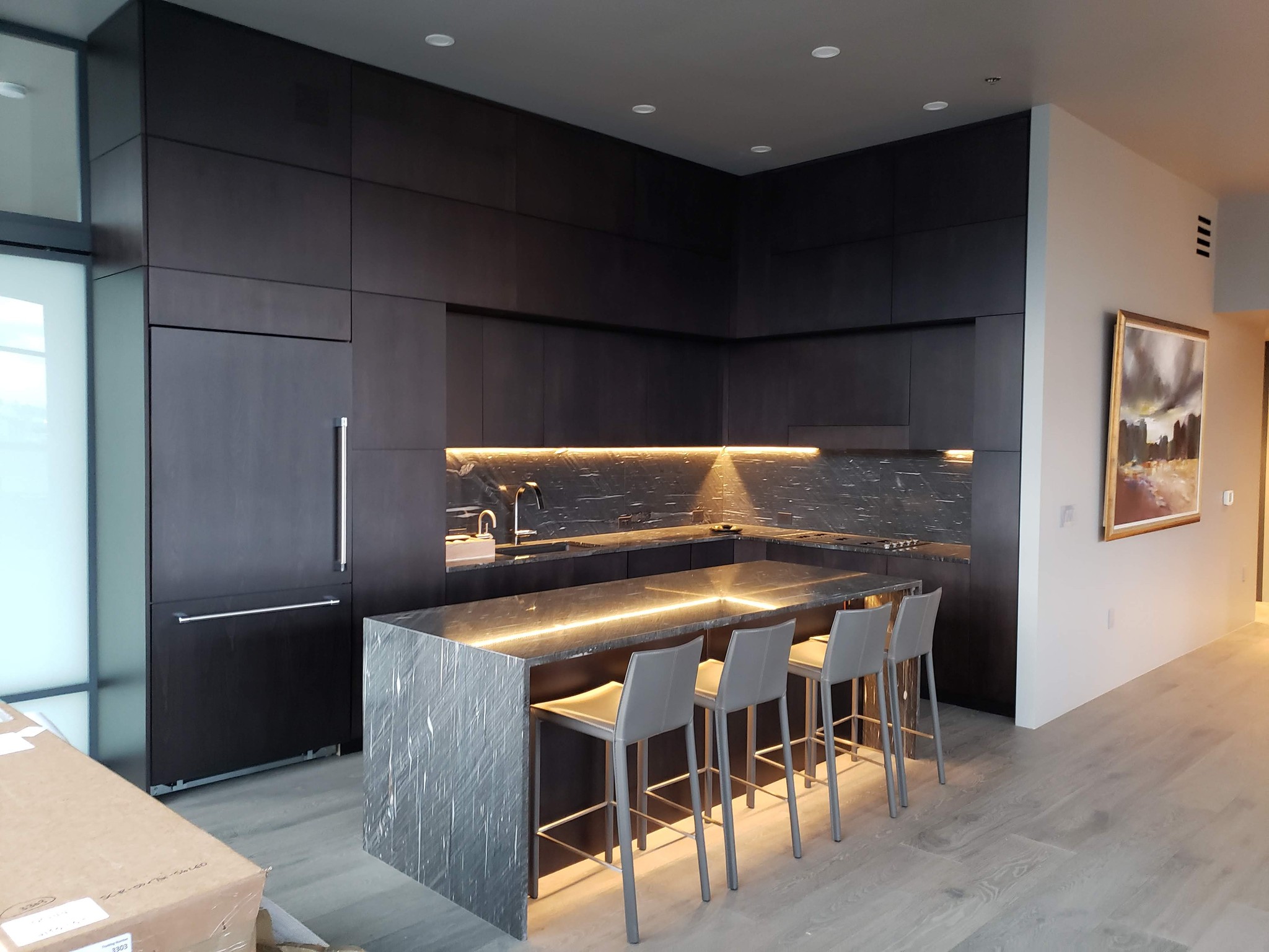 Modern kitchen with dark cabinetry, a gray island, and minimalist decor, featuring stylish lighting and wall art.