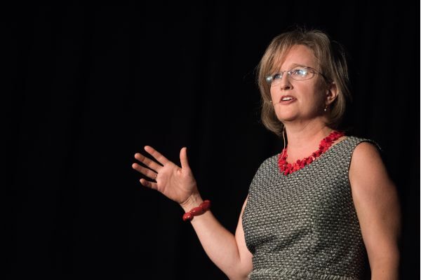 Elise Partin giving a talk with hand raised, mid speech, dark black background