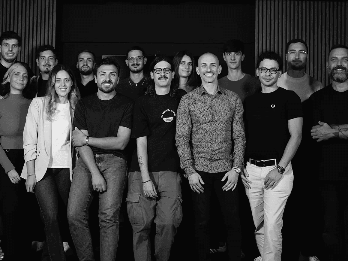 A large group photo of diverse team members gathered in an industrial-style space with arched ceiling.