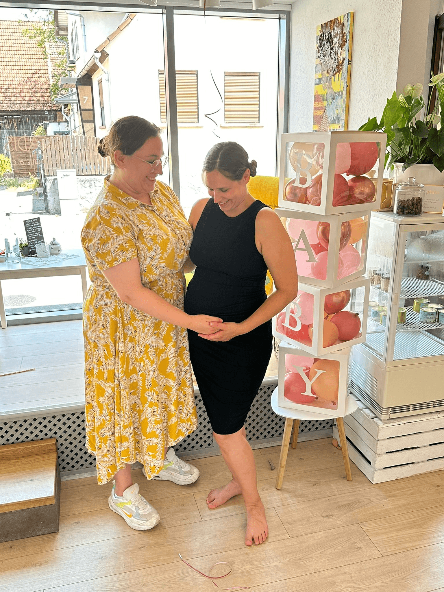 Angela von Studio Unico und ihre Schwester legen auf der Babyparty gemeinsam die Hände auf den Babybauch und lächeln.