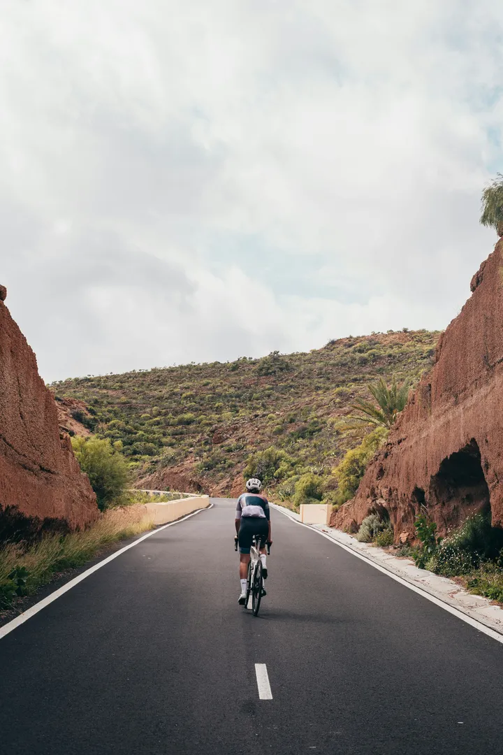 Cycliste sur route grimpant un col sur une route asphaltée parfaite bordée de falaises rouges.