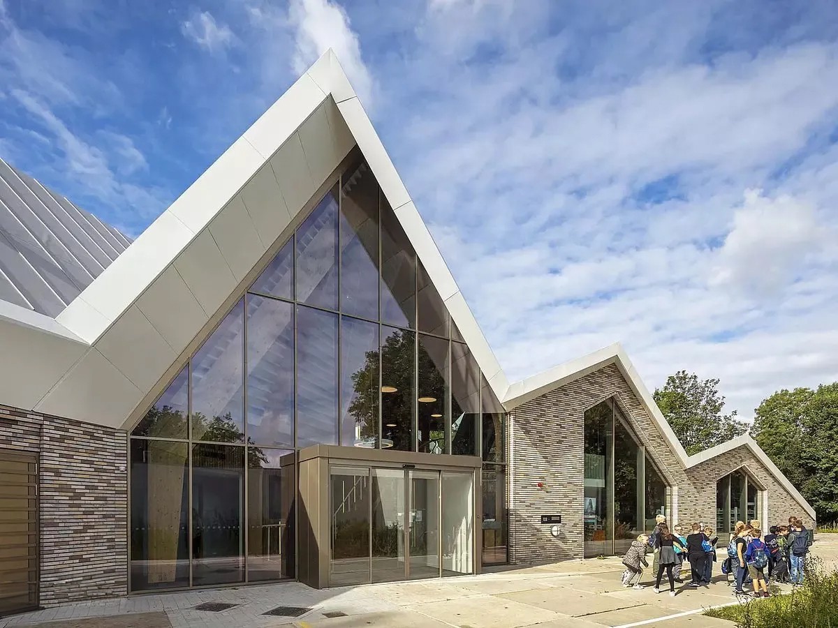 Modern gebouw met glazen gevel en puntgevel, schoolklas buiten.