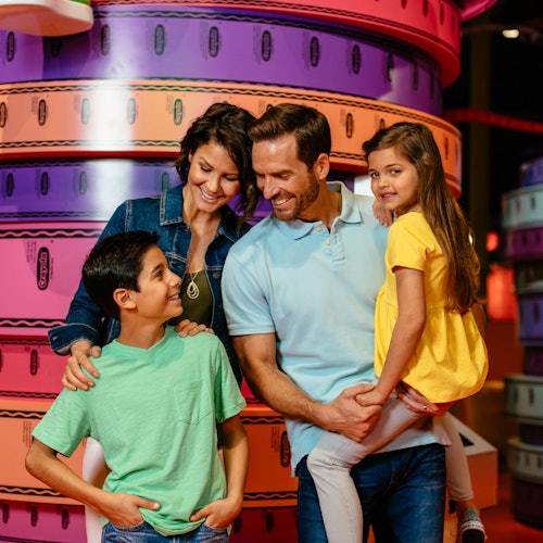 一家四口面帶微笑，站在一堆大型多彩的膠帶卷前。