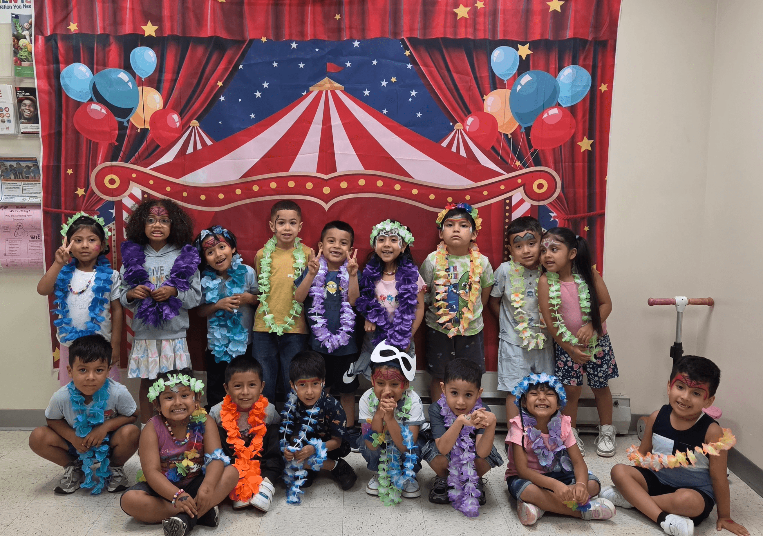 Preschoolers decked out in leis in front of a carnival backdrop.