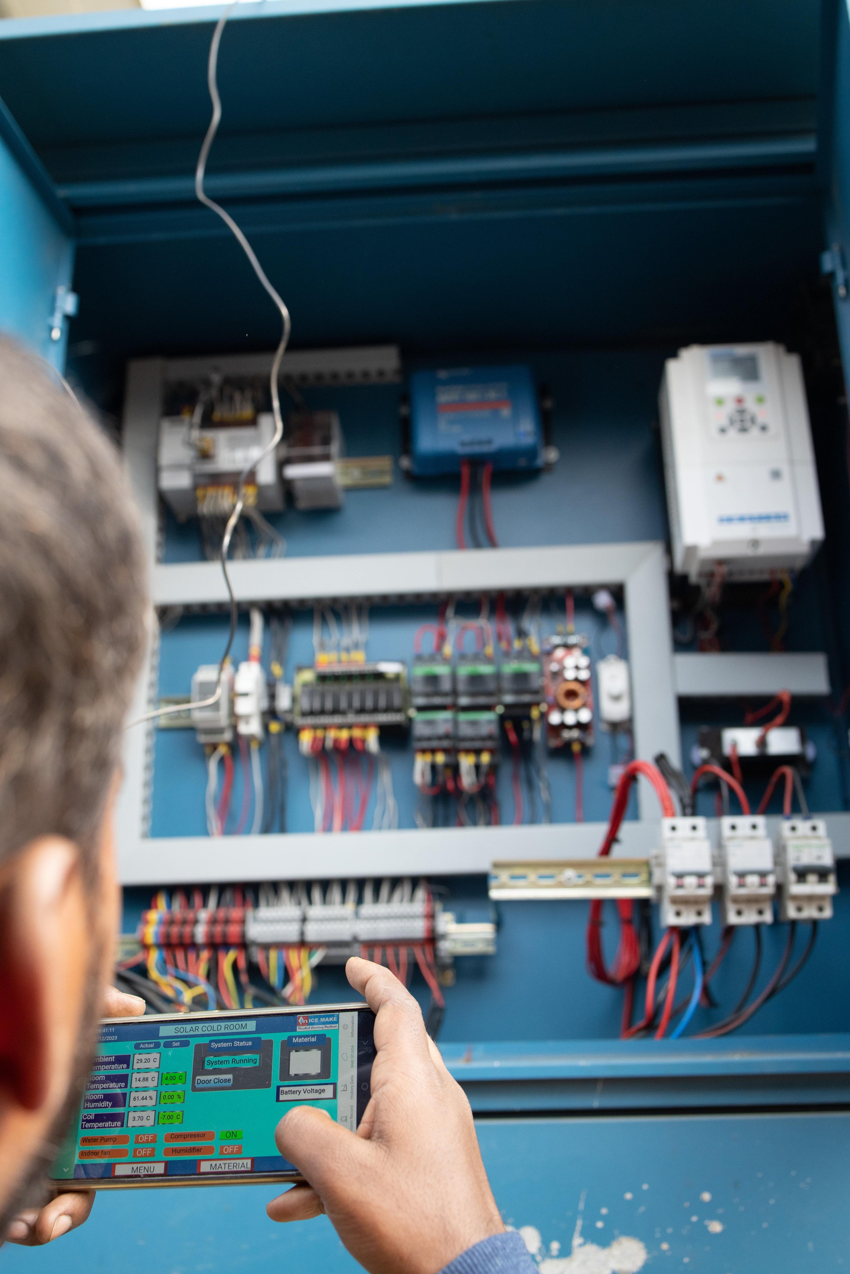 Sunmeister engineer in front of the solar cold room control panel monitoring everything regarding the cold room from an app through his phone