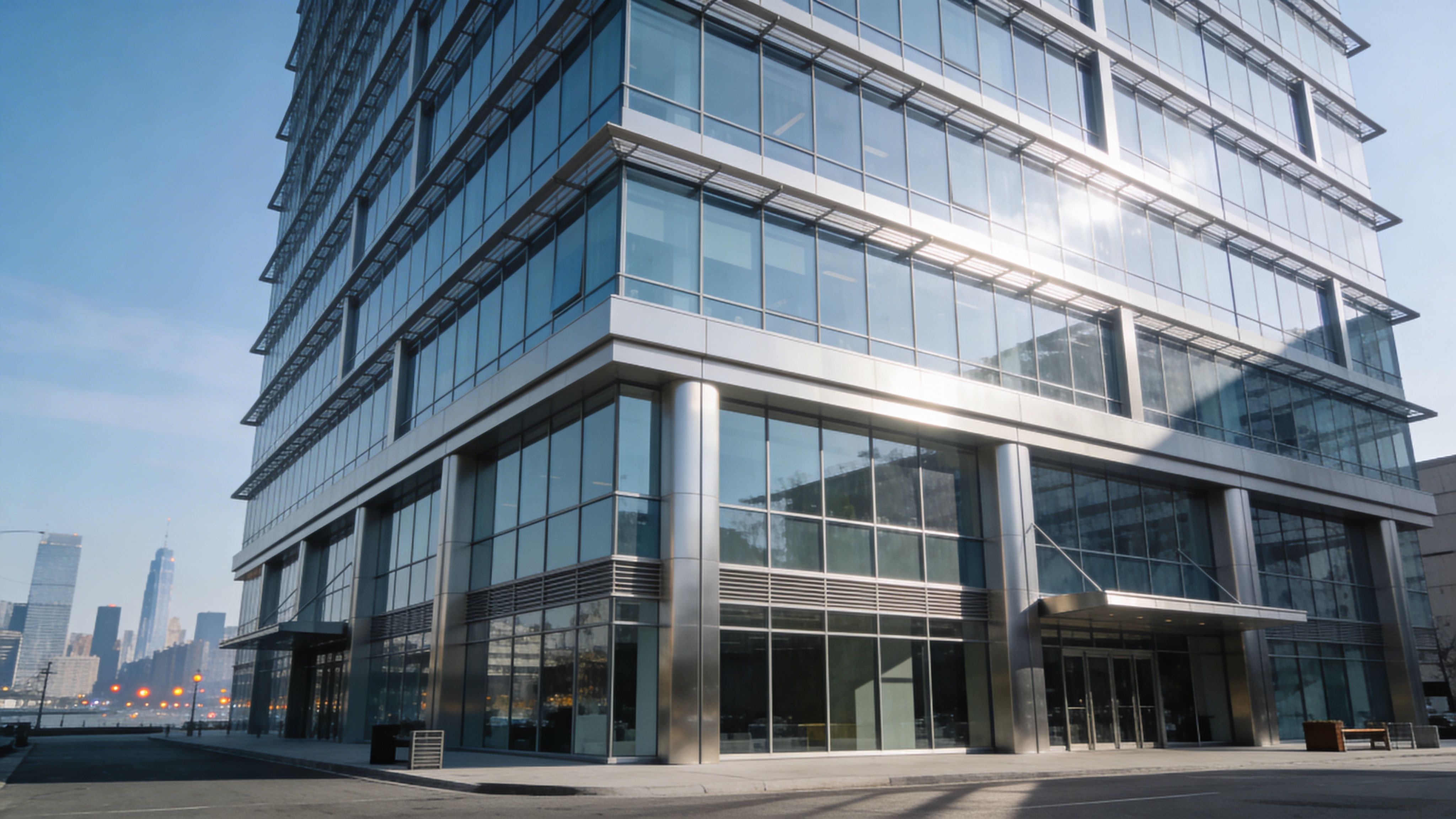 Exterior view of a modern glass office building with urban skyline backdrop and corporate architecture