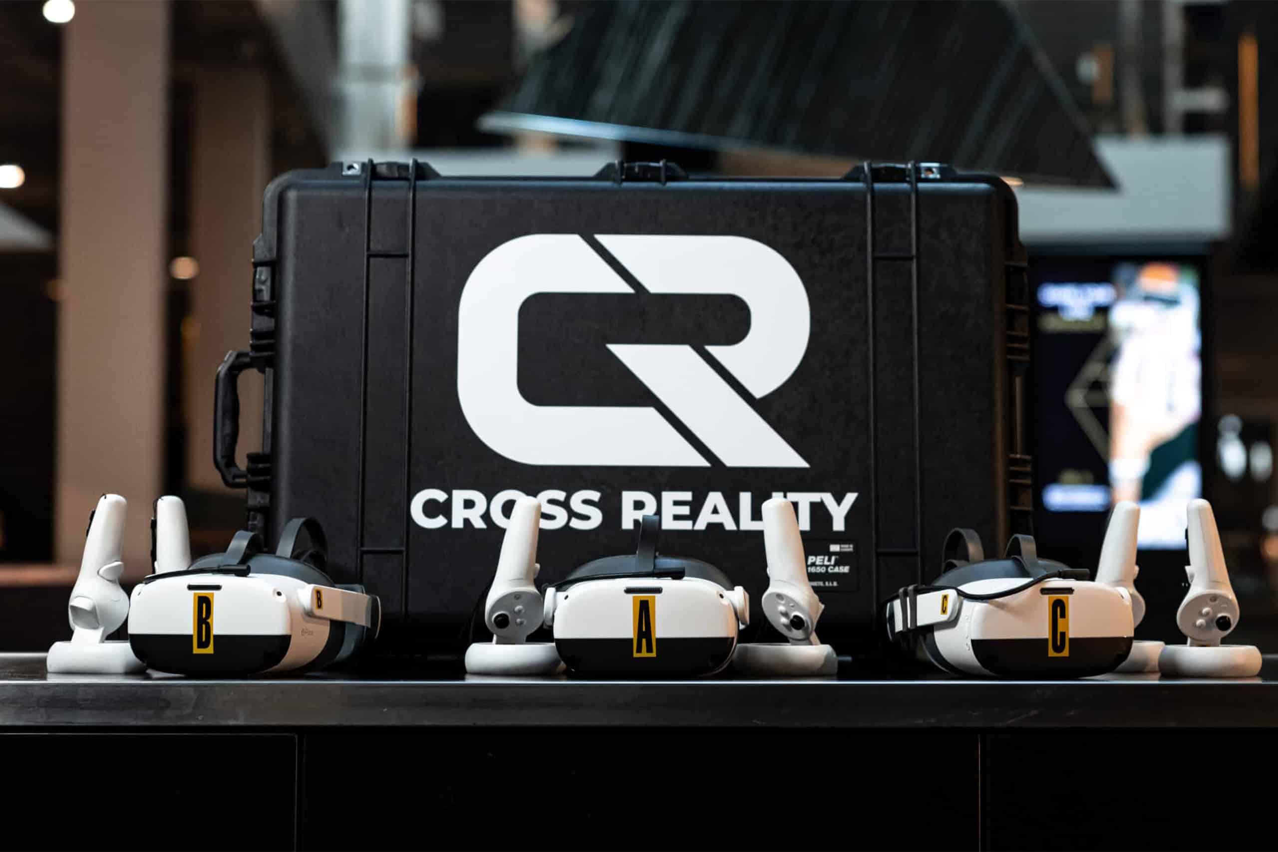 A young person with curly hair smiles at the camera while sitting in front of a laptop against a dark background.