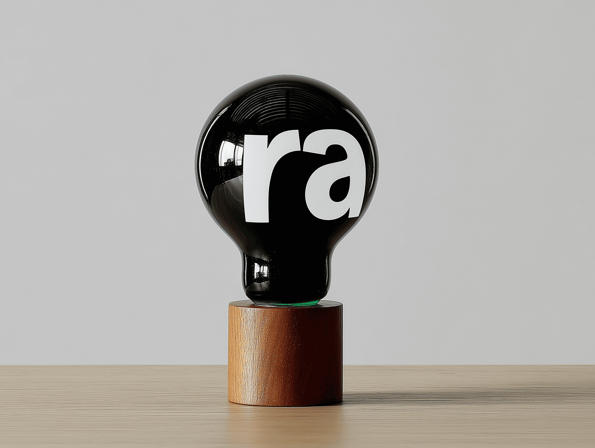 Minimal black lightbulb sculpture with bold white lettering, displayed on a cylindrical wooden base against a neutral background.