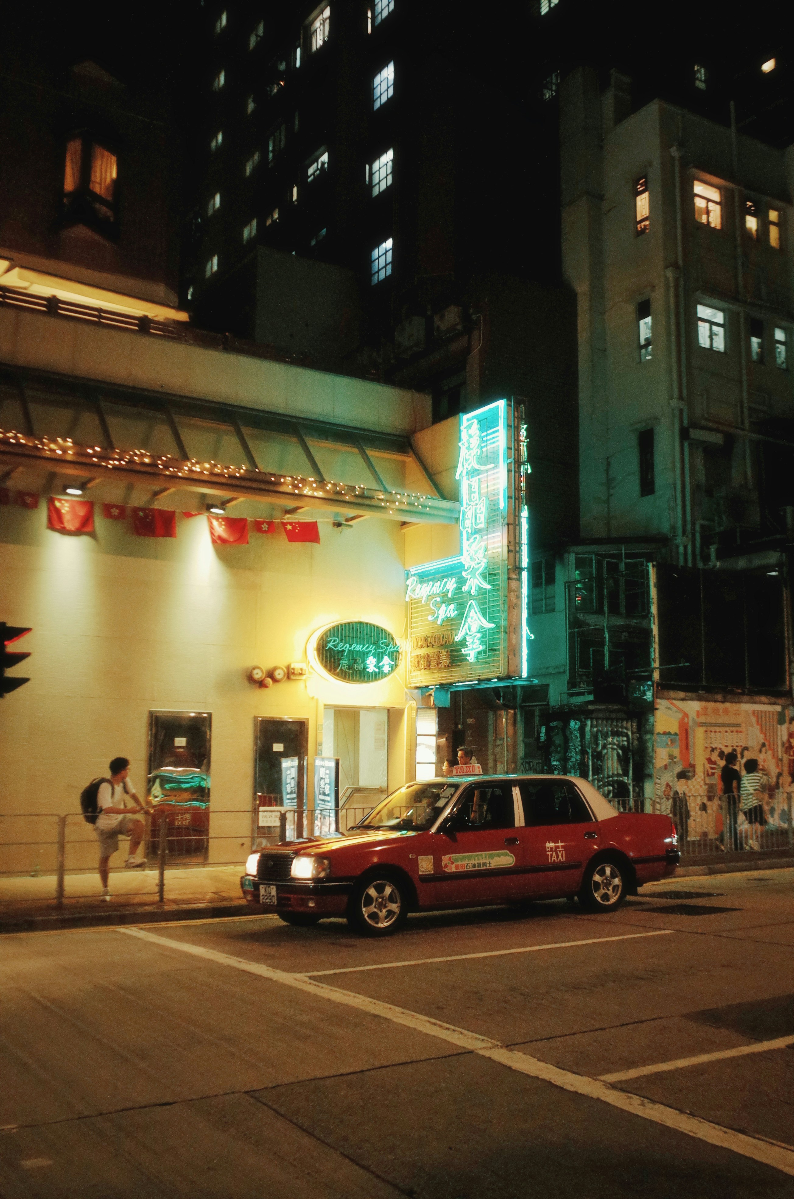 Red taxi drives down a street at night.