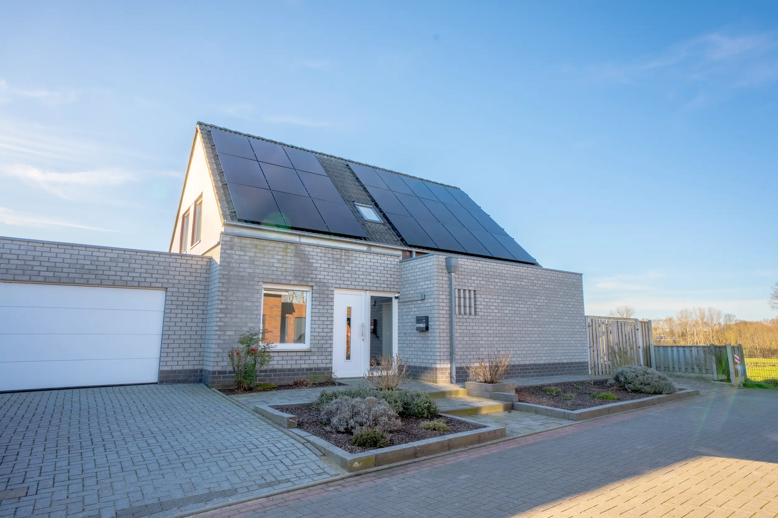 Frontansicht eines Einfamilienhauses in Ochtrup mit gepflastertem Vorgarten, weißer Garage und Solaranlage auf dem Dach bei blauem Himmel