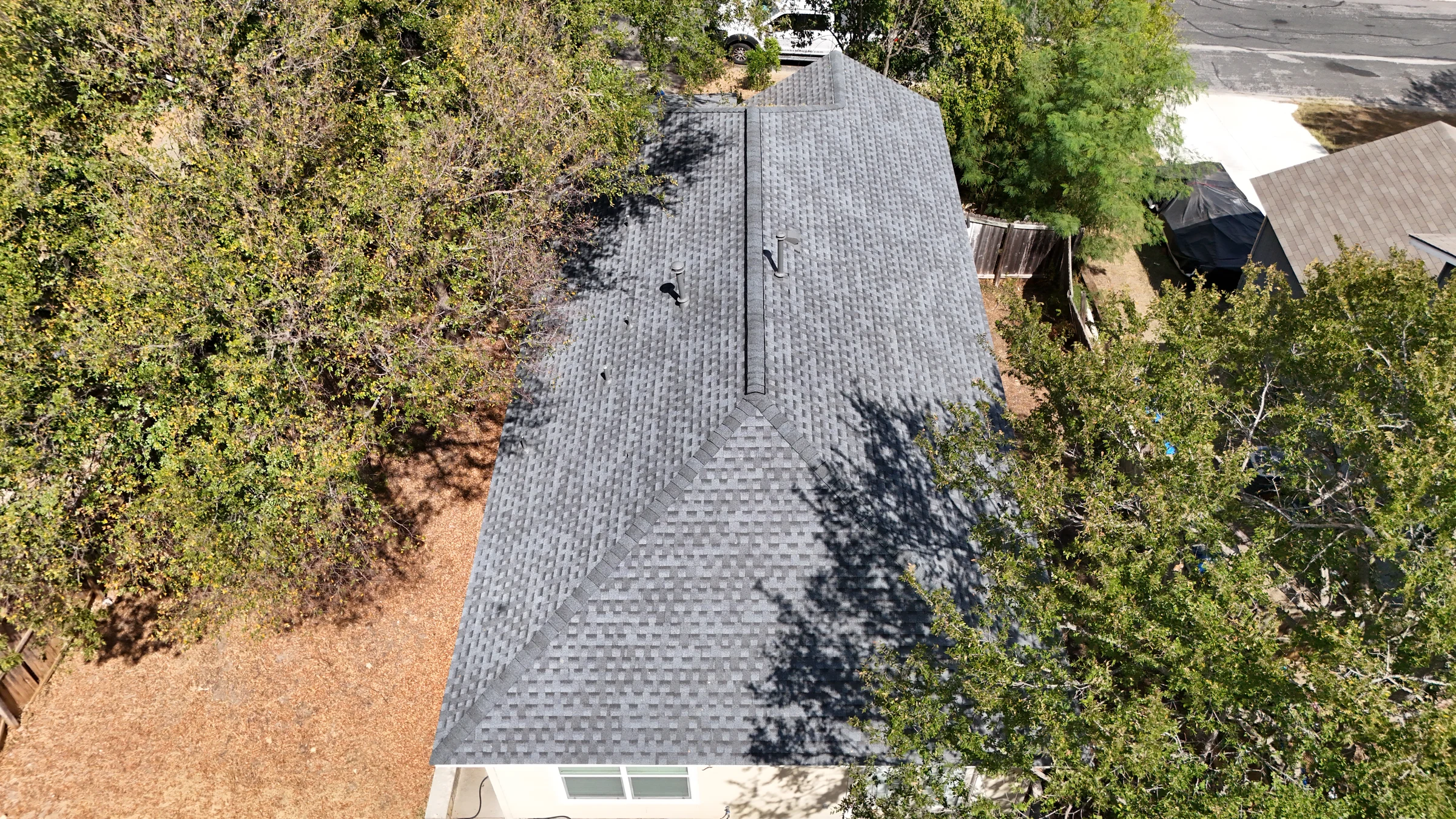 Rear aerial view of the finished Austin shingle roof, showing the hip roof and long ridge vent.