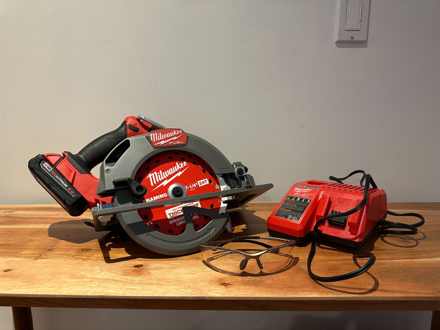 Scie circulaire sans fil Milwaukee FUEL 7-1/4 po avec chargeur, batterie M18 et lunettes de protection, posée sur une table en bois