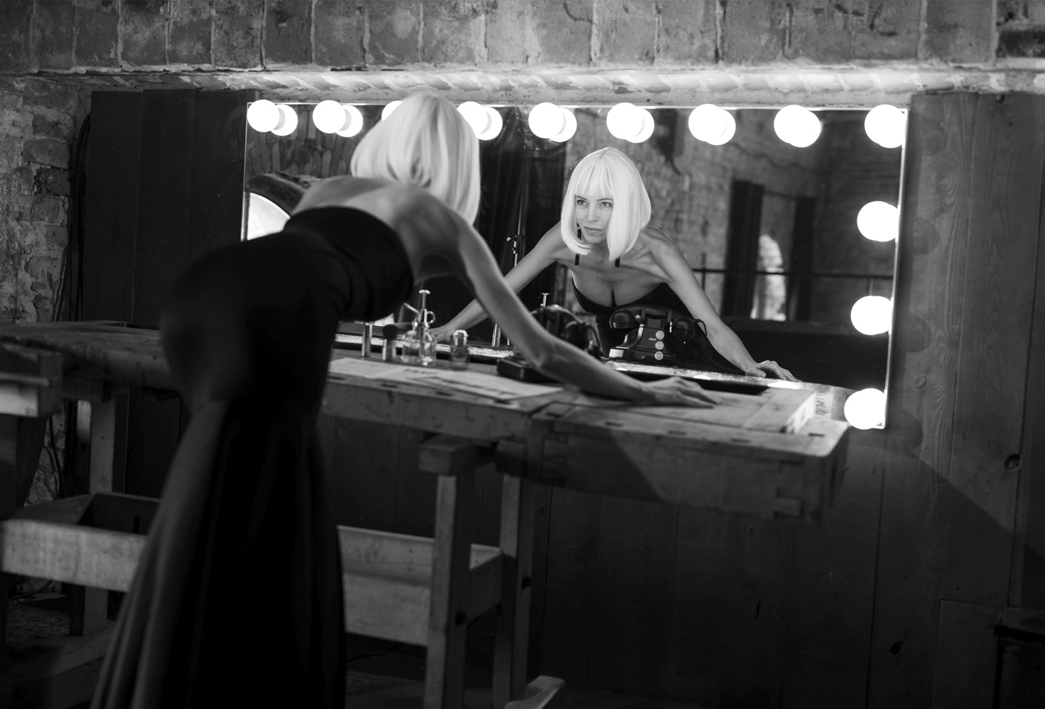 Woman at a dressing table with lights, black coat, black and white - The Space Between Roles - Agnieszka Czyzkowska Photography