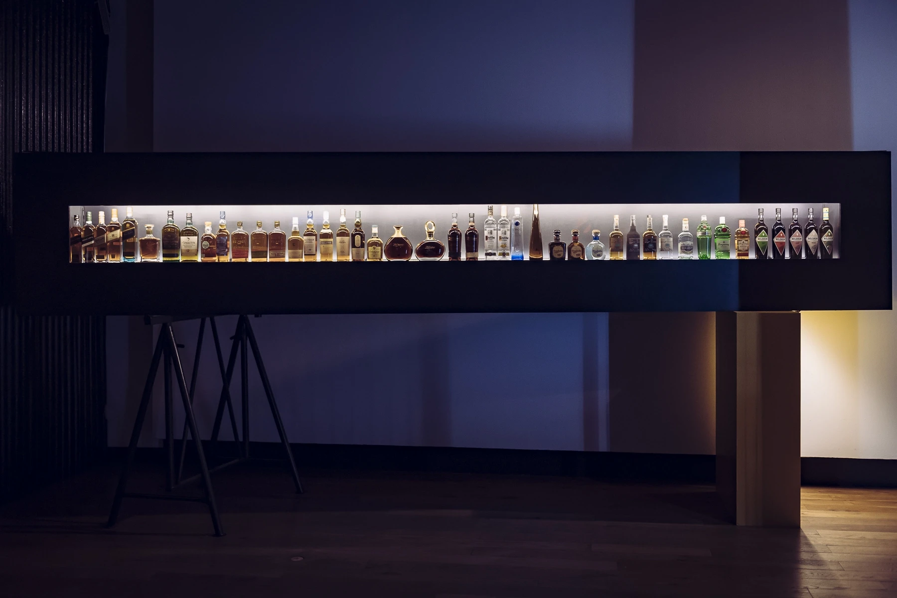 Long backlit display case on tripod legs at DIAGEO BCB19 with a row of whisky, vodka and gin bottles in warm light.
