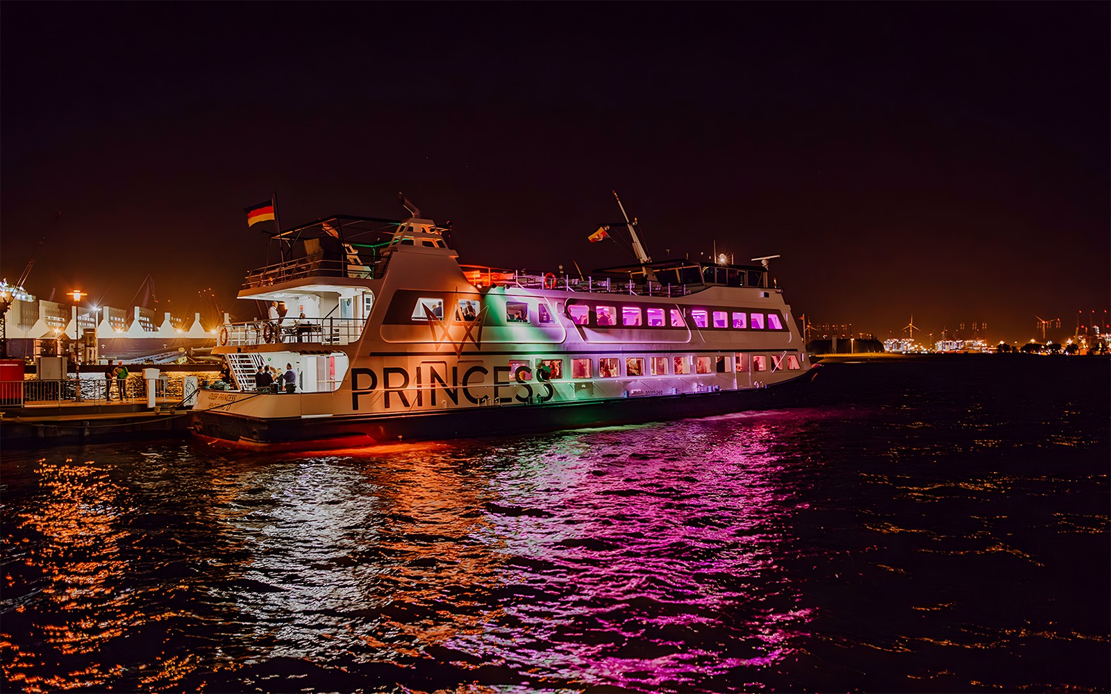 Large ship illuminated with colorful lights during evening cruise.