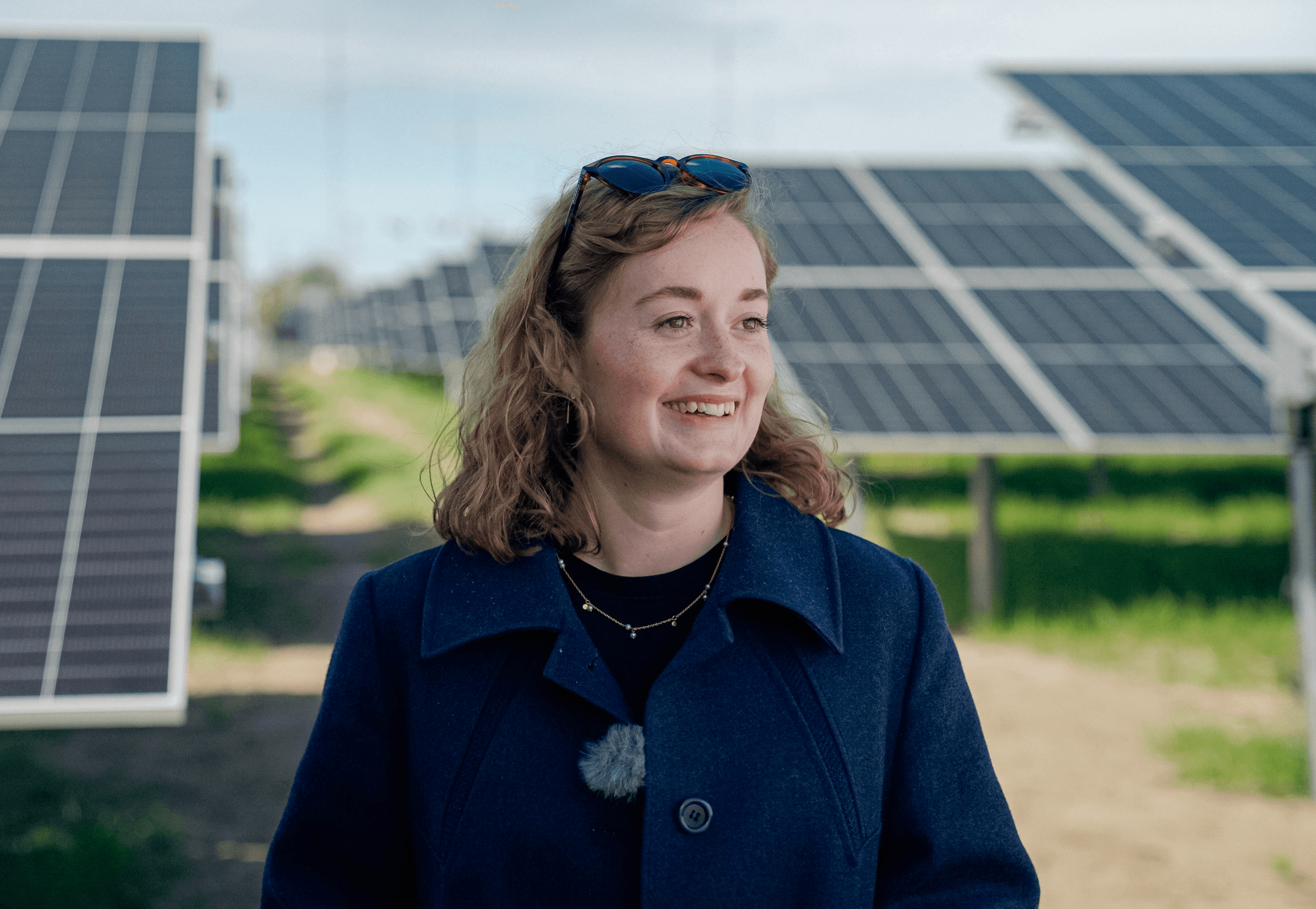 Woman with blonde hair standing and smiling in front of a field of solar panels.