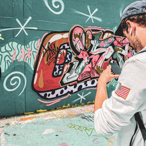 穿着带有美国国旗贴布的白色夹克的男子在拍摄绿色墙面上五颜六色的涂鸦。