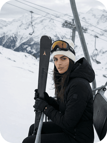 Woman carrying skis on her shoulder, standing in a snowy mountain environment
