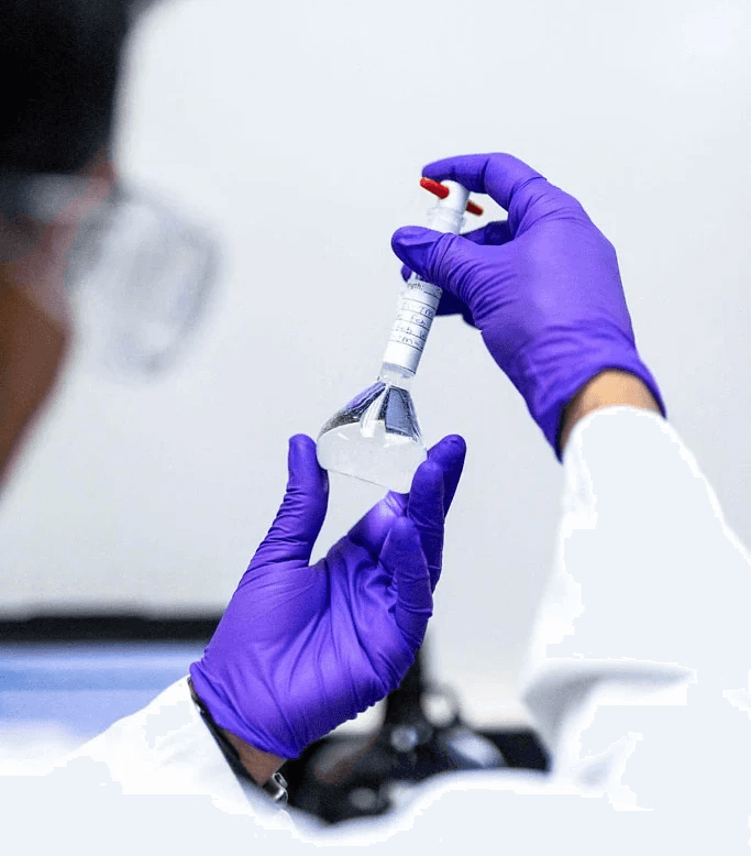 Close-up of a scientist wearing gloves carefully handling a labeled flask in a laboratory.