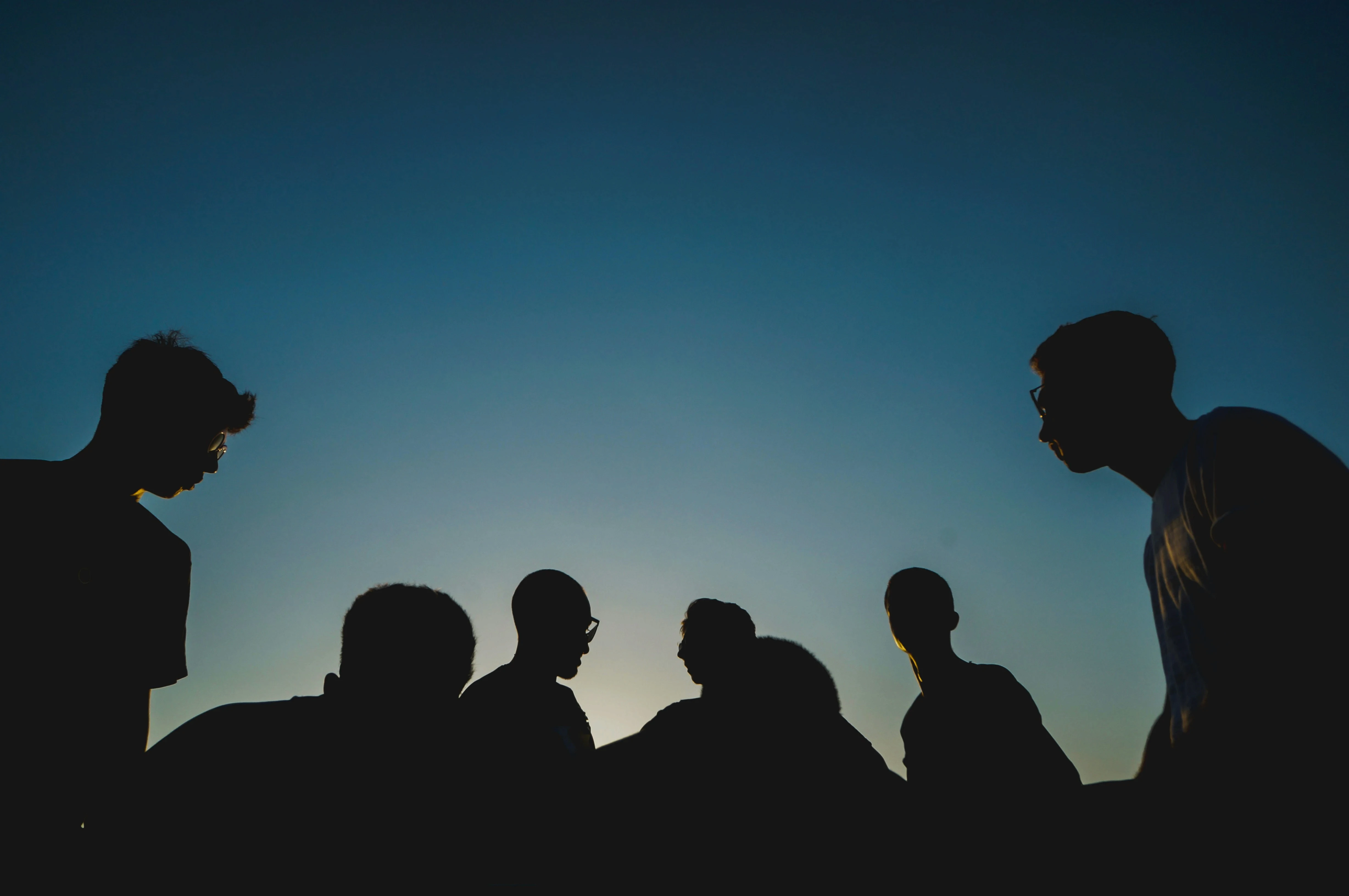 Silhouettes of men in a group at dusk, representing male social dynamics, emotional distance, and connection struggles