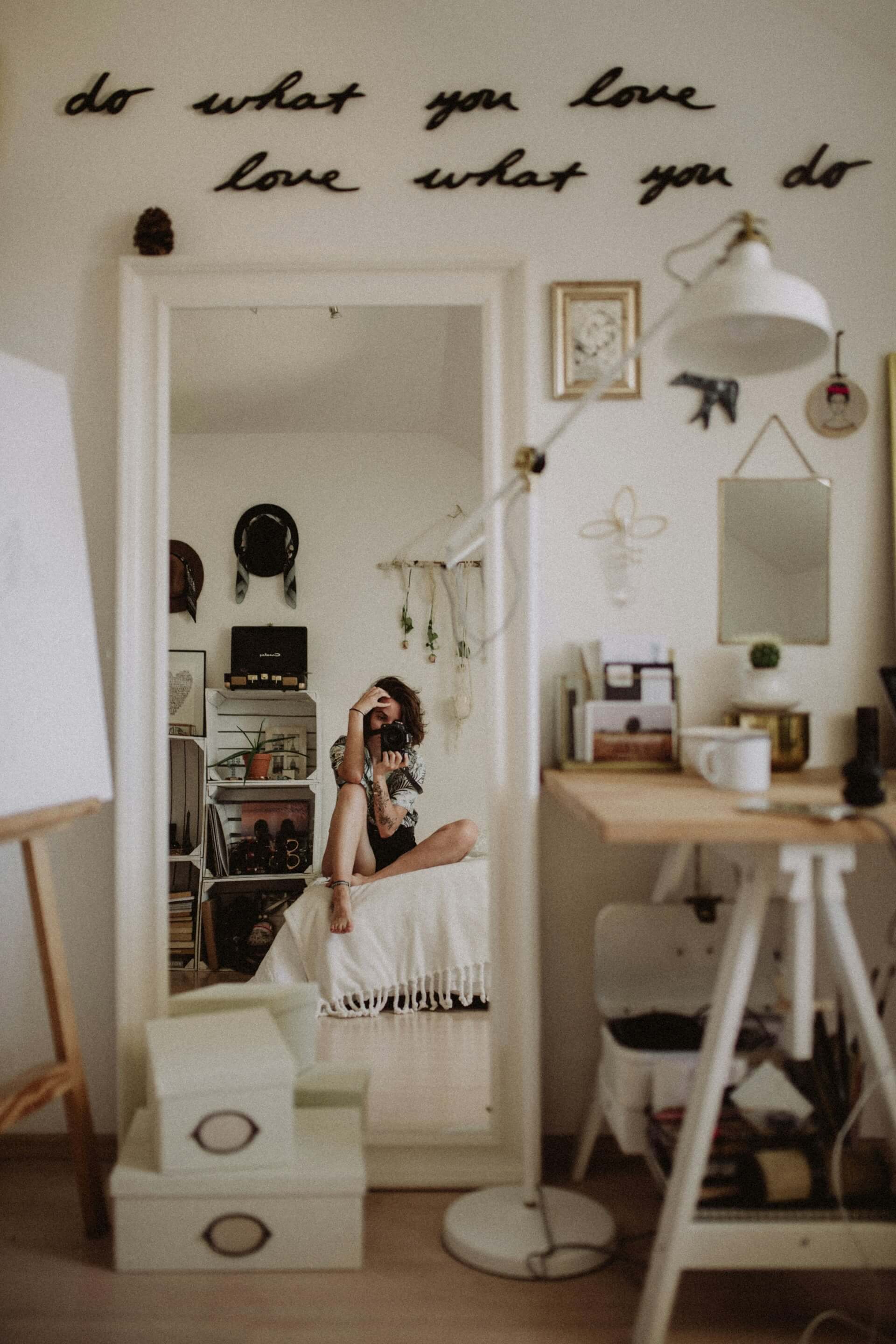 A woman poses for a selfie in her bedroom, highlighting her cheerful demeanor amidst a comfortable and stylish setting