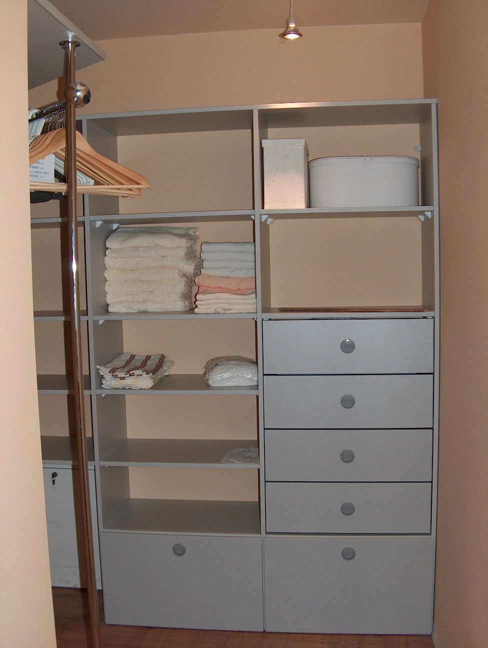 Wnętrze garderoby na wymiar z ergonomicznym systemem półek, drążków na wieszaki oraz pojemnych szuflad w kolorze jasnoszarym.