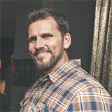Headshot of Jonathan Bristow smiling in a plaid shirt