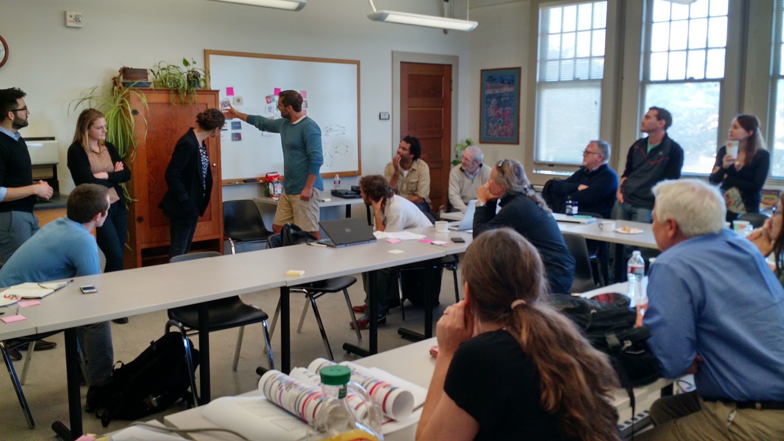 Group of workshop collaborators gathered around a whiteboard, classifying sticky notes as part of a guided brainstorm at Stanford University.