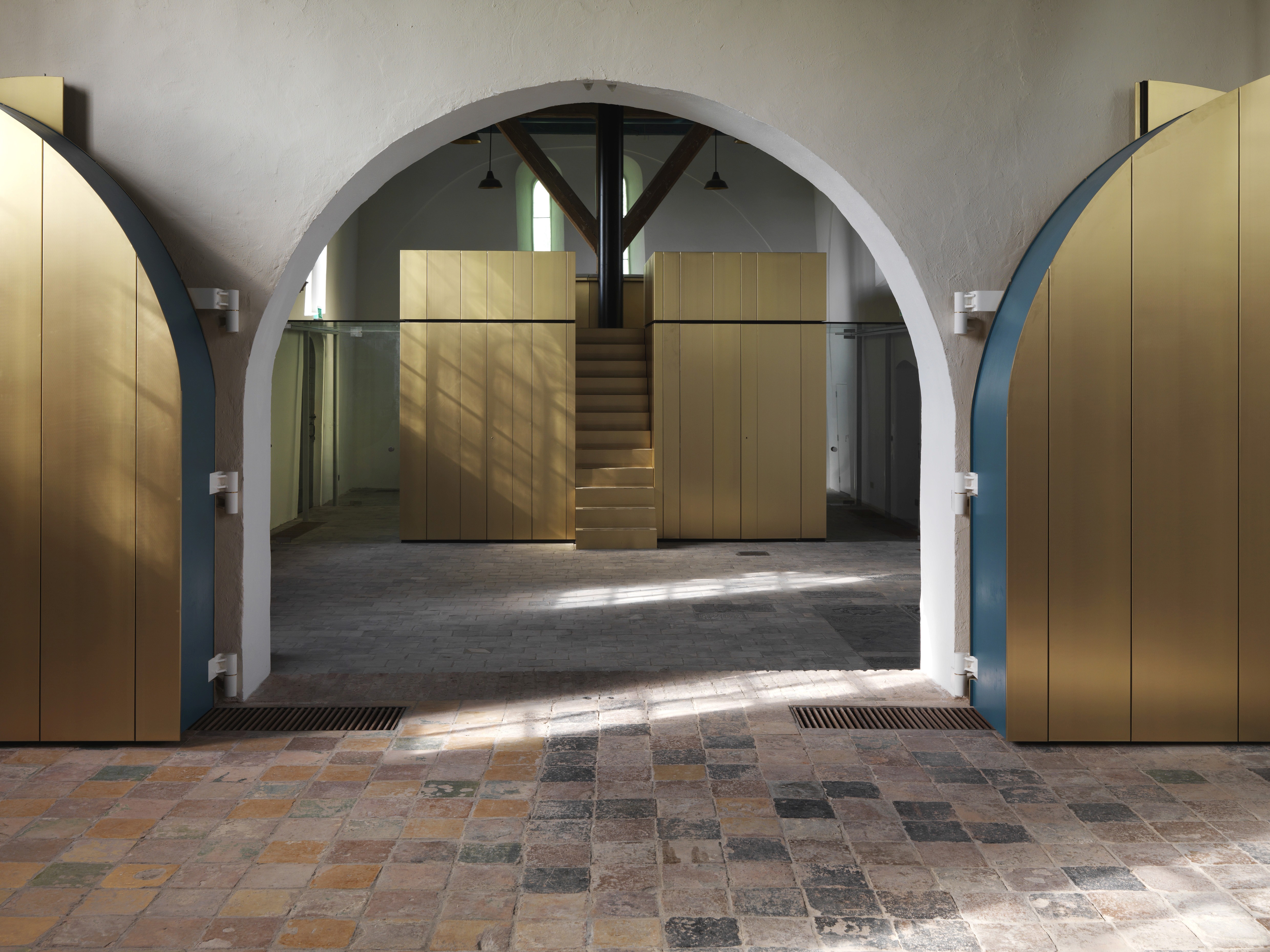 Interieur met boogdoorgang, gouden kastjes, trap en bakstenen vloer.