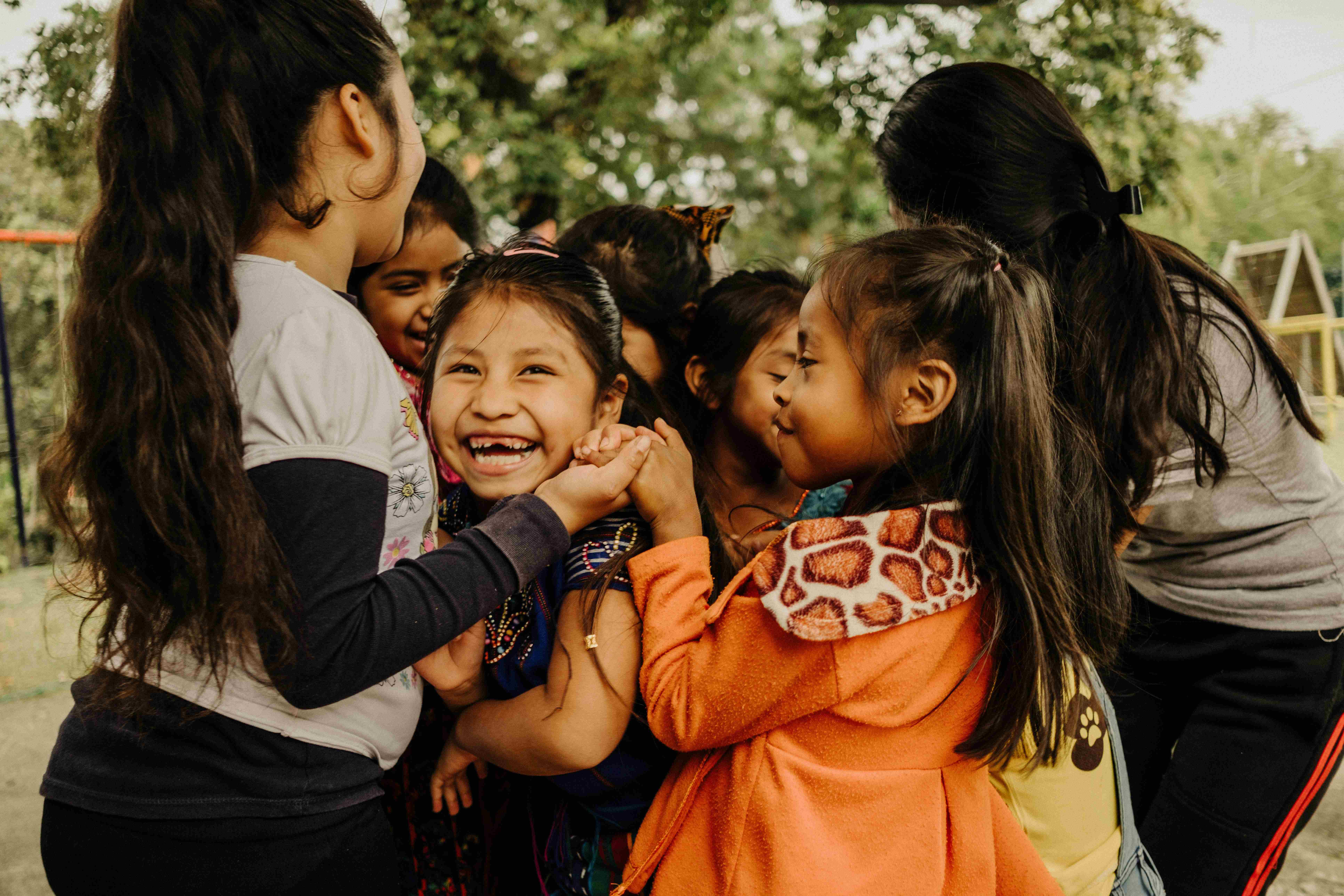 Smiling young girls embrace and laugh together outdoors, reflecting the joy and community fostered by faith-based care.
