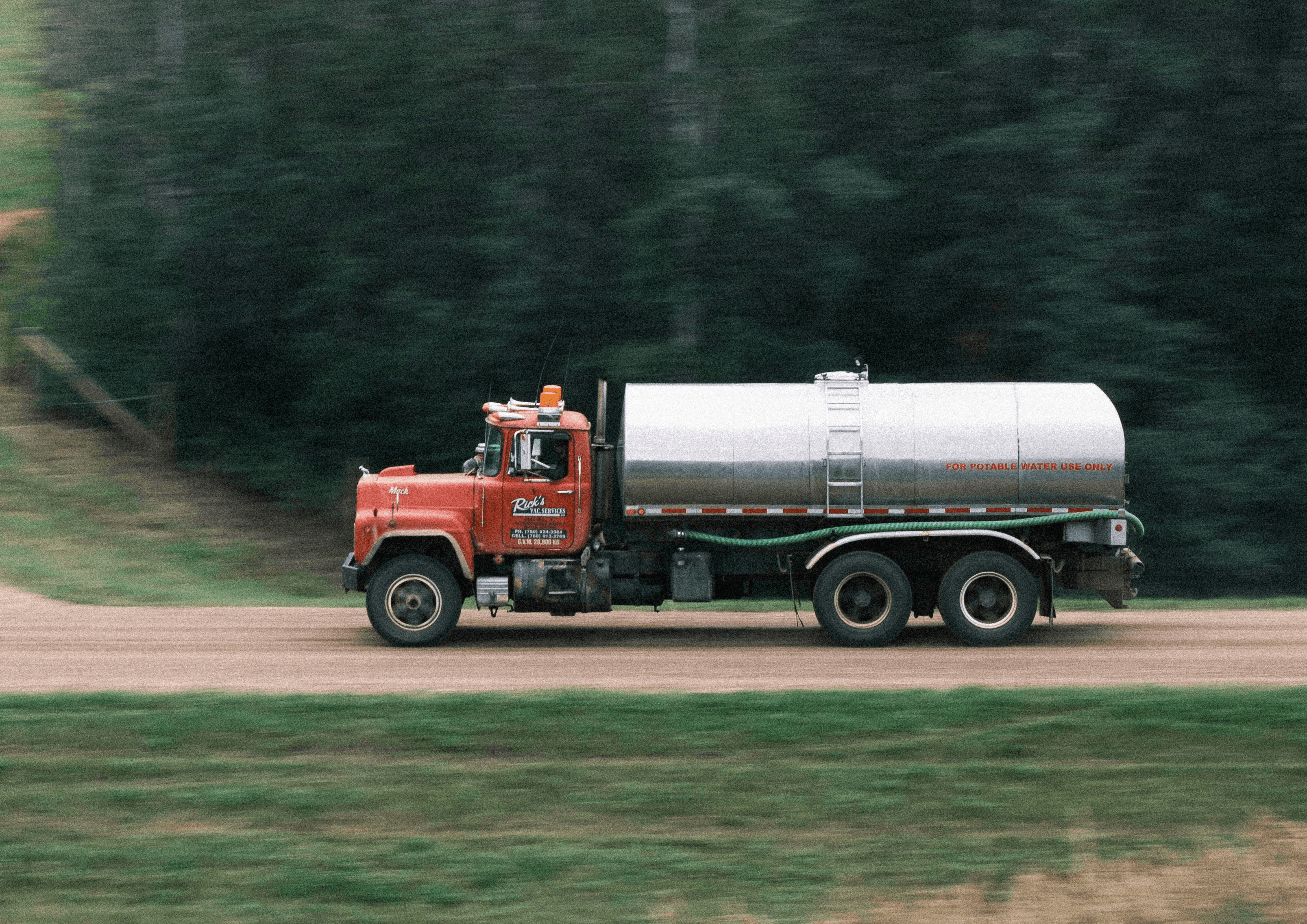 Red tanker truck driving along a dirt road.