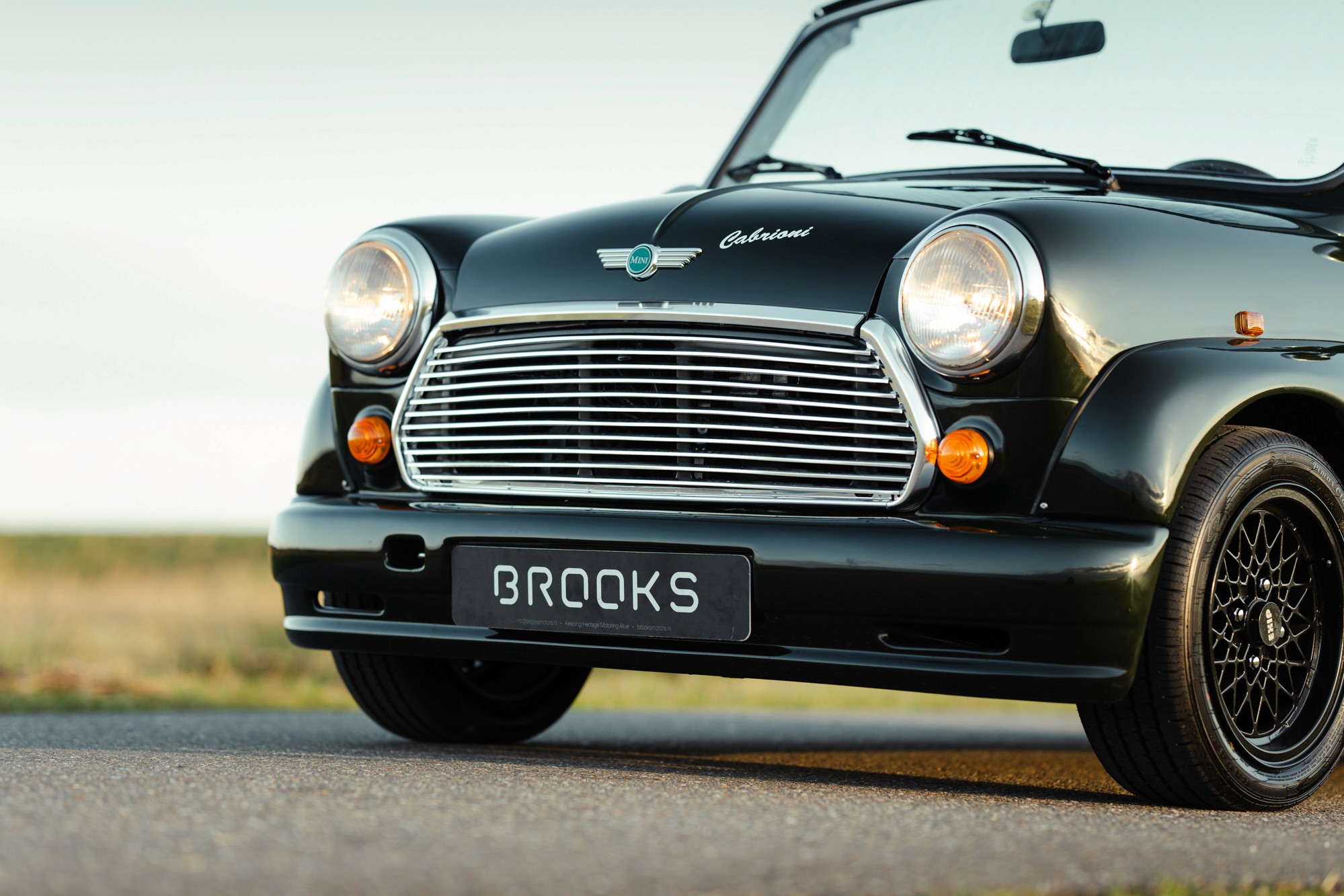 Dark green mini classic cabriolet on a road, front view.