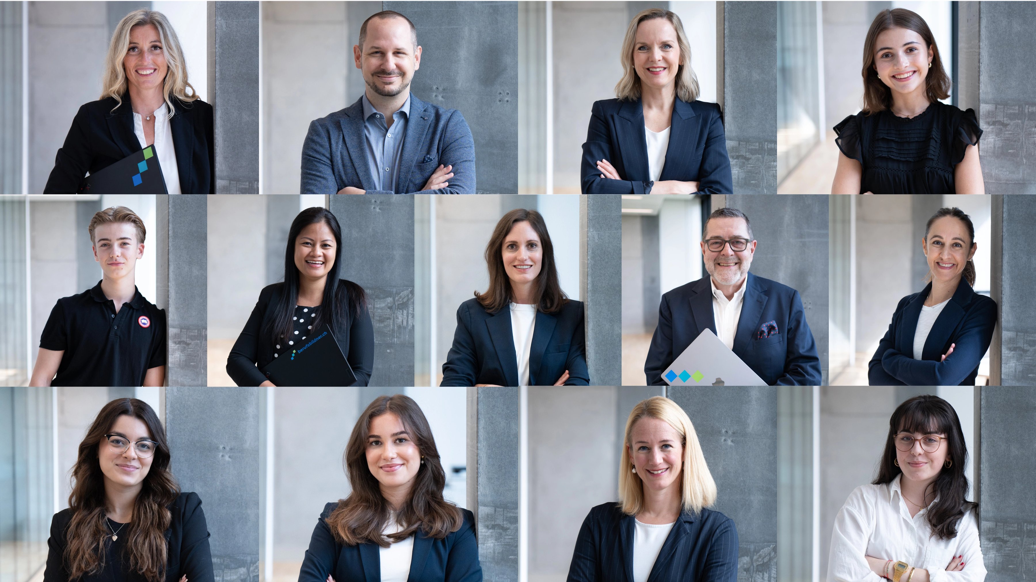 A young person with curly hair smiles at the camera while sitting in front of a laptop against a dark background.
