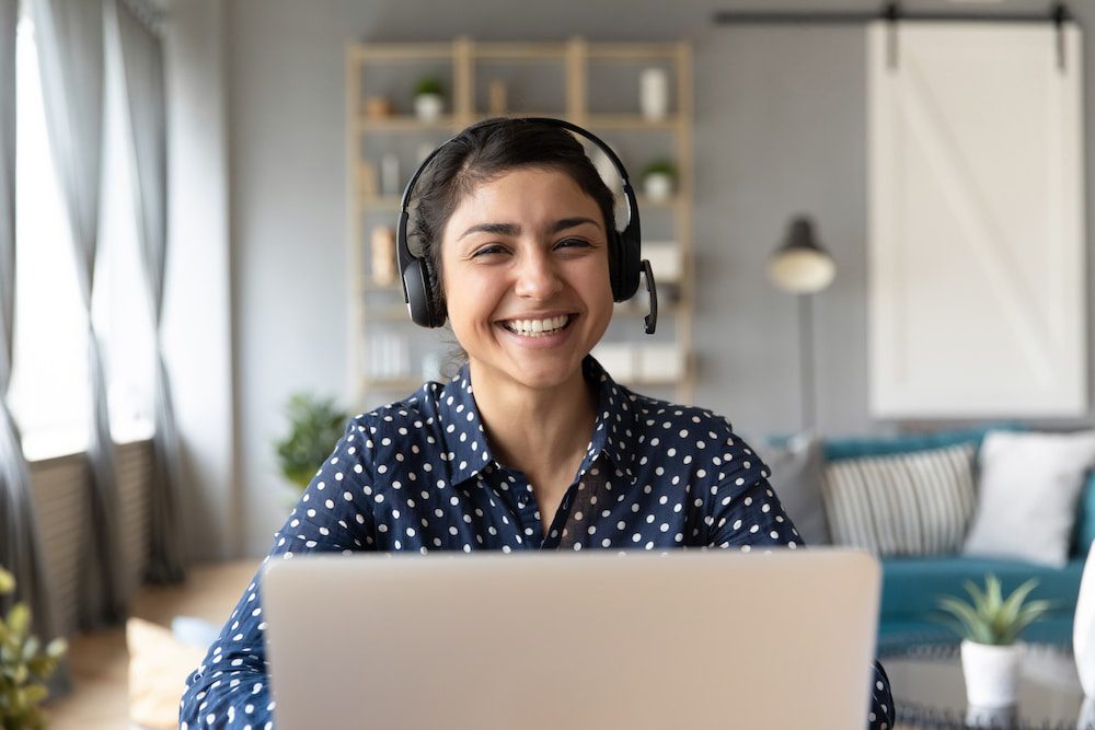 Smiling woman wearing headset working on laptop in home office.