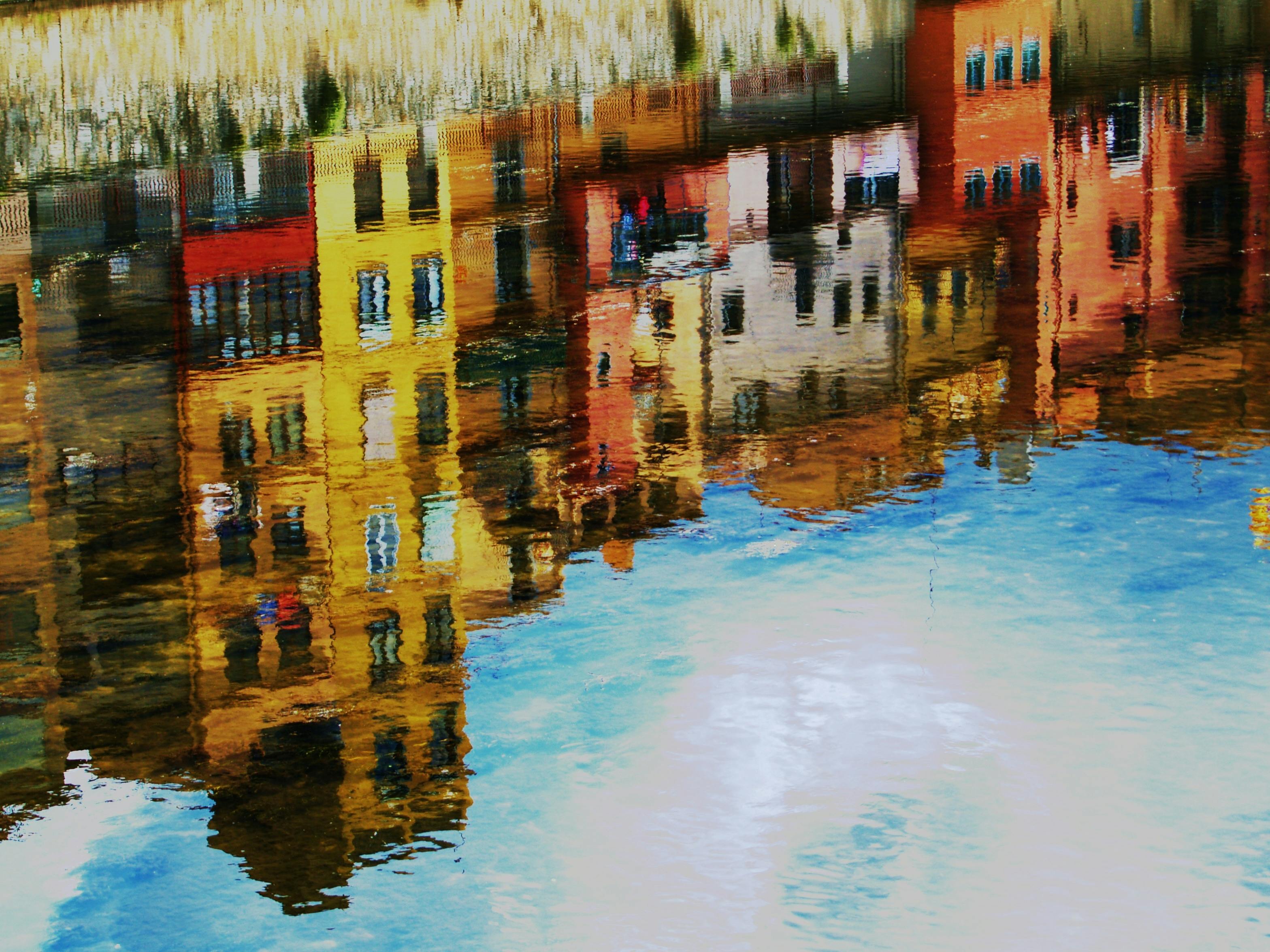 Colorful buildings reflected in rippling water, creating a distorted and painterly effect