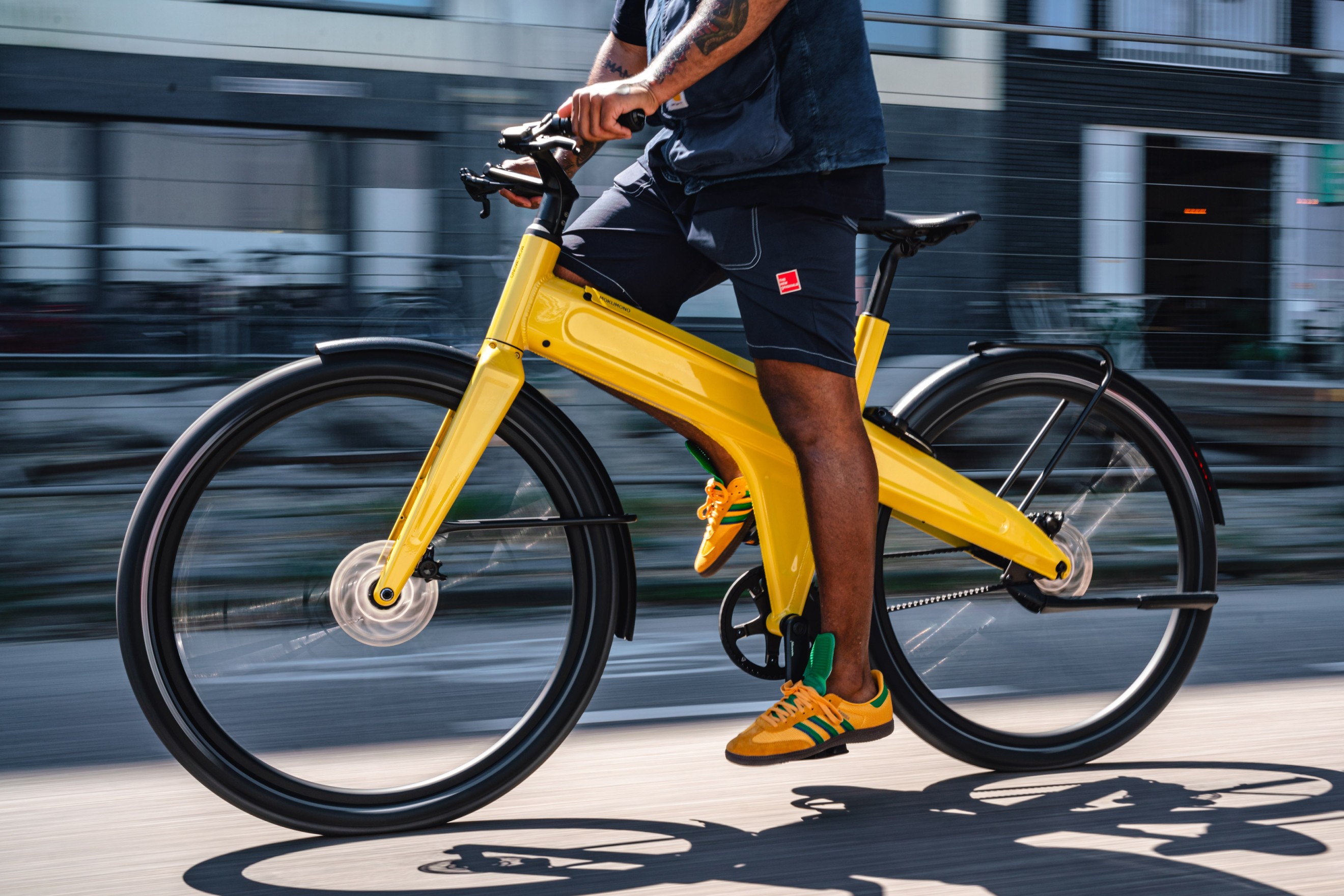 Mokumono yellow bike speeding through Amsterdam, captured with a slow shutter speed to create a dynamic motion blur that emphasizes its high-speed ride.