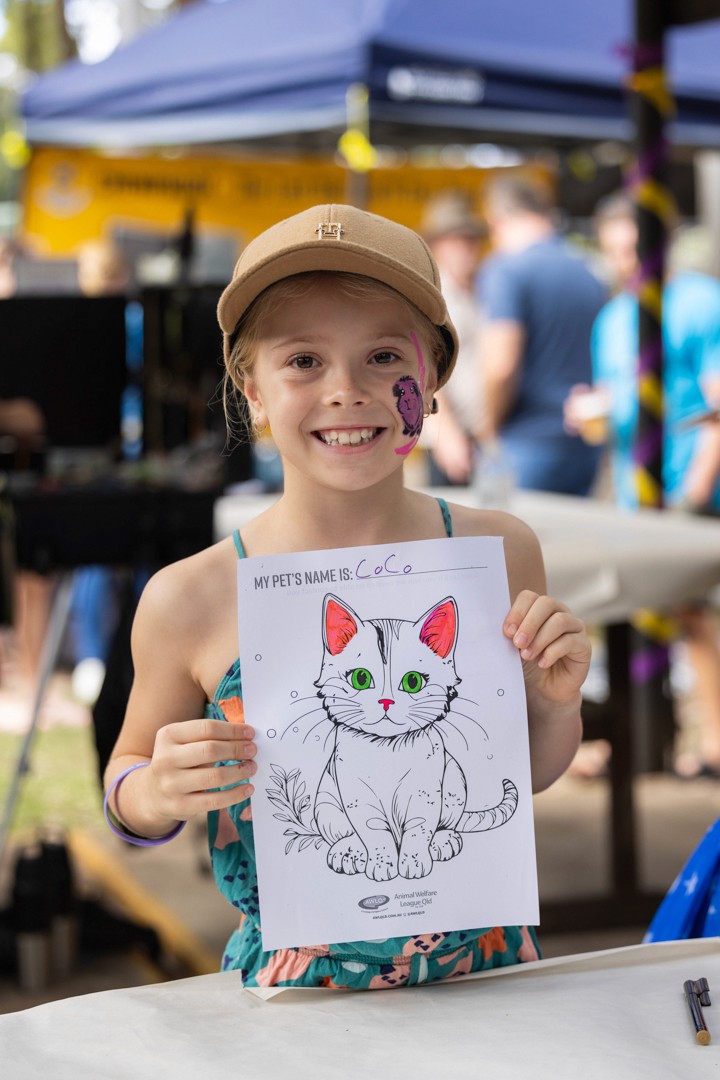 Girl with face paint holding up cat colouring-in picture