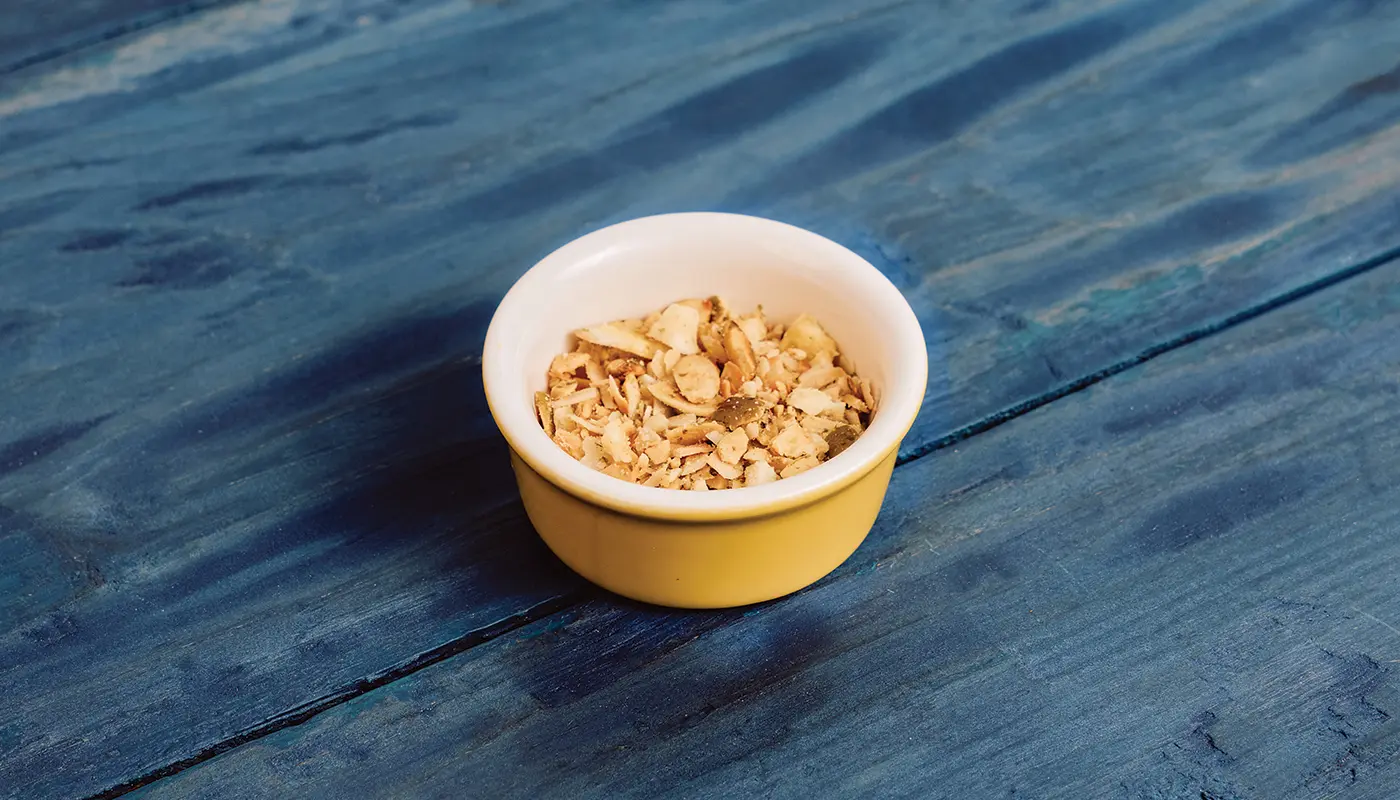 Coconut crunch in a small yellow dish on blue wooden boards.