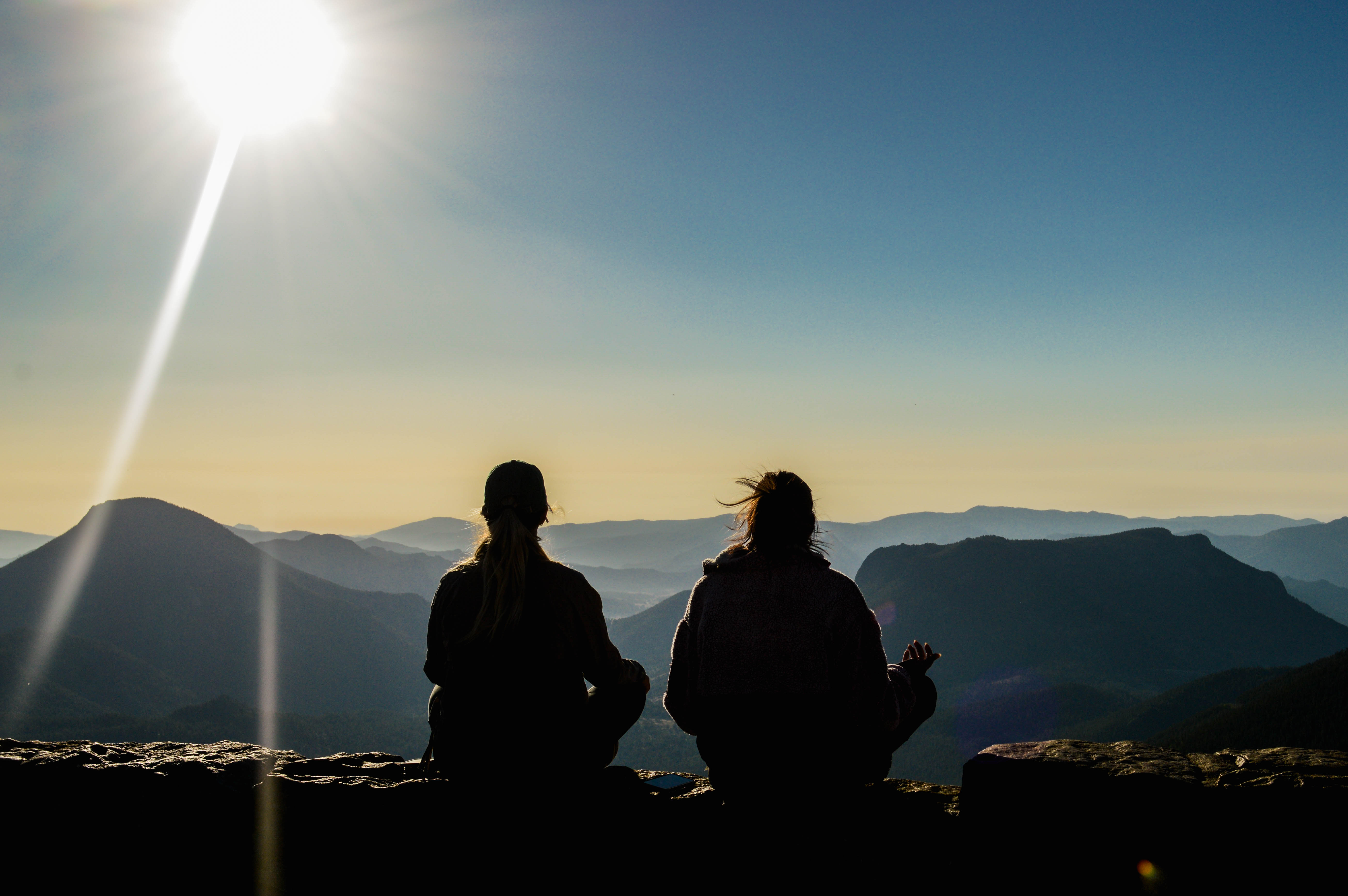 Two people sitting in meditation overlooking mountain scenery, representing calm, breath, and nervous system regulation.