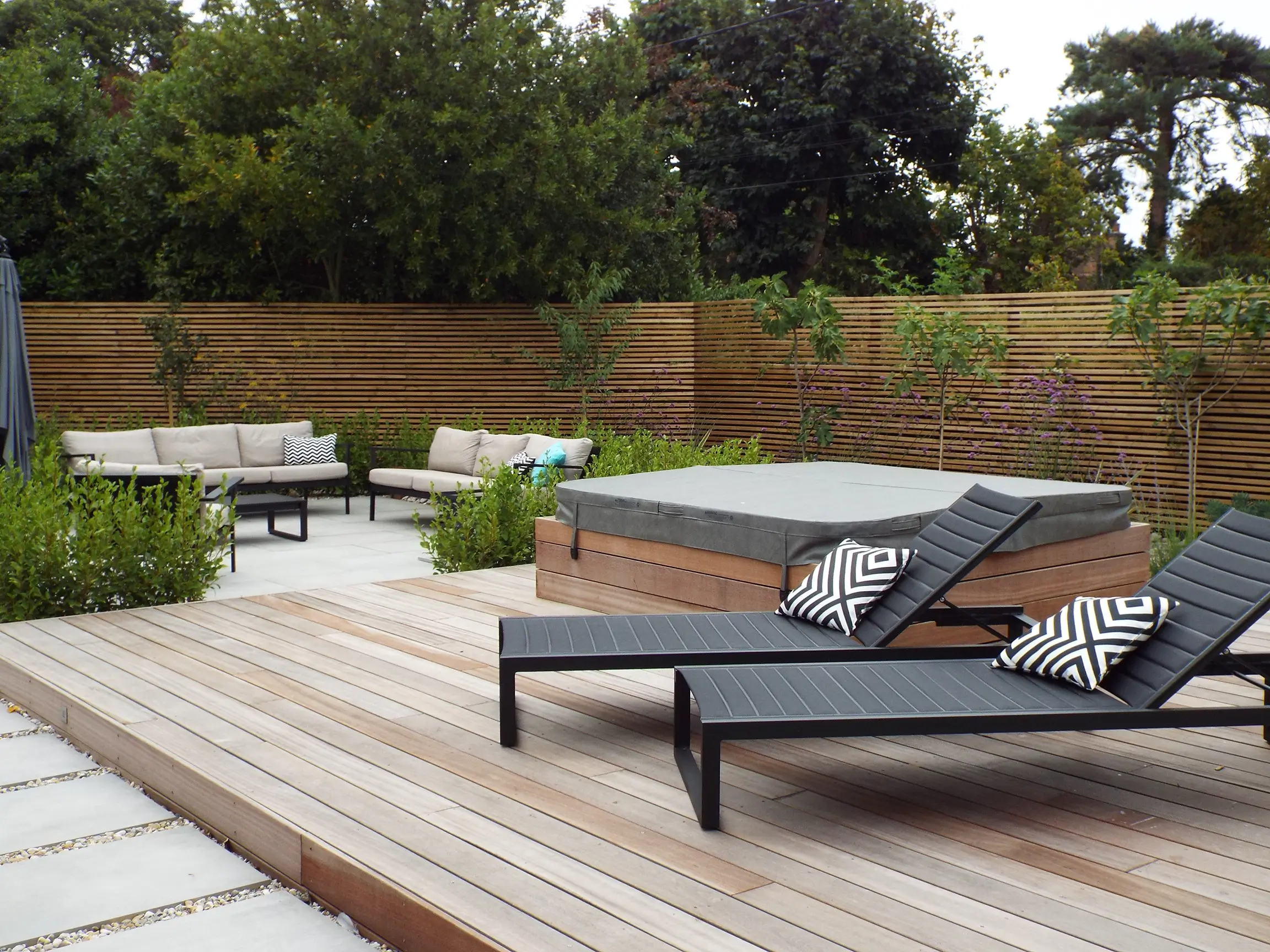 A modern outdoor patio featuring lounge chairs, a dining area, and greenery in a serene setting.