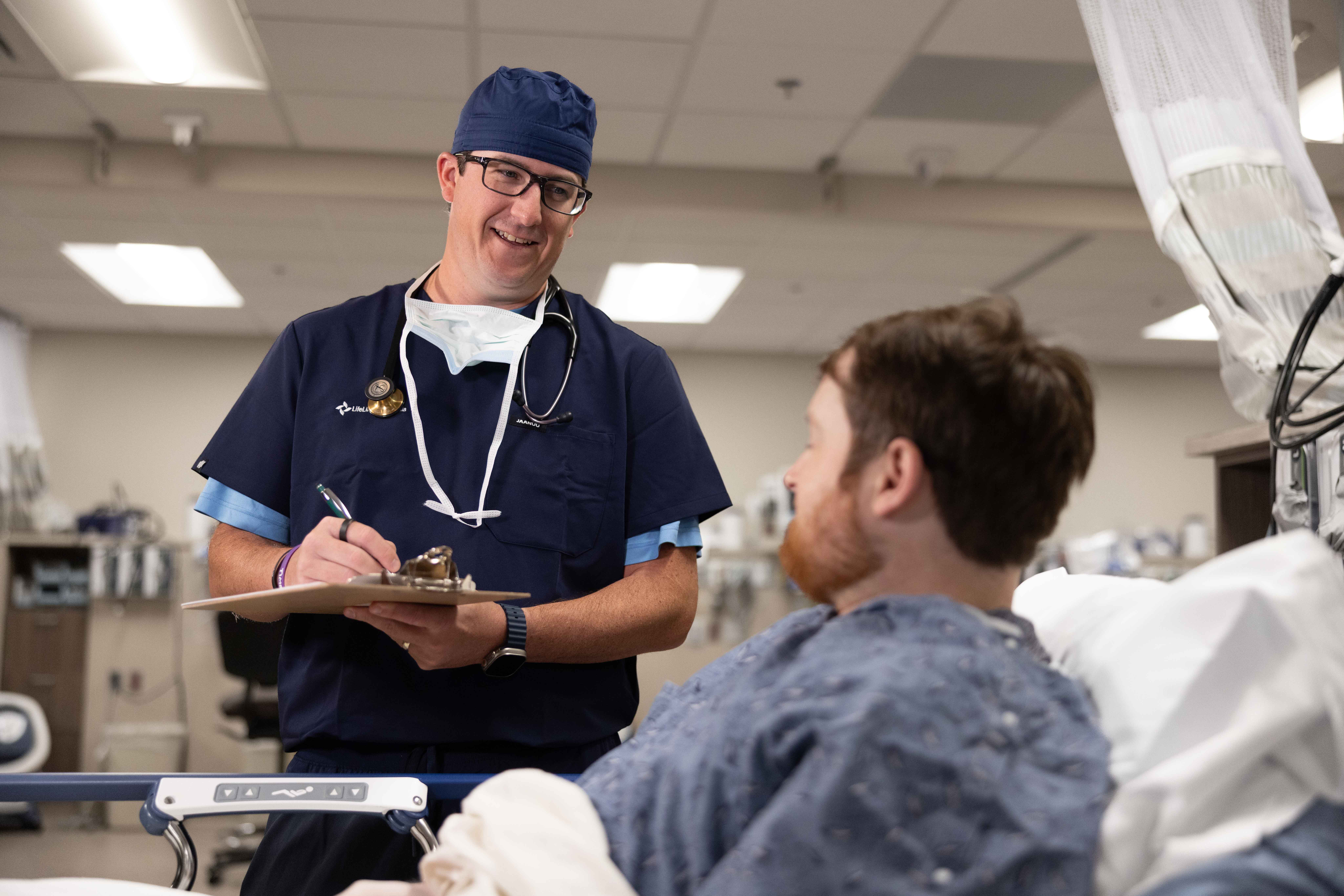 An anesthesia provider consults with a patient bedside, clipboard in hand, reflecting LifeLinc's commitment to clinical excellence and consistent patient outcomes