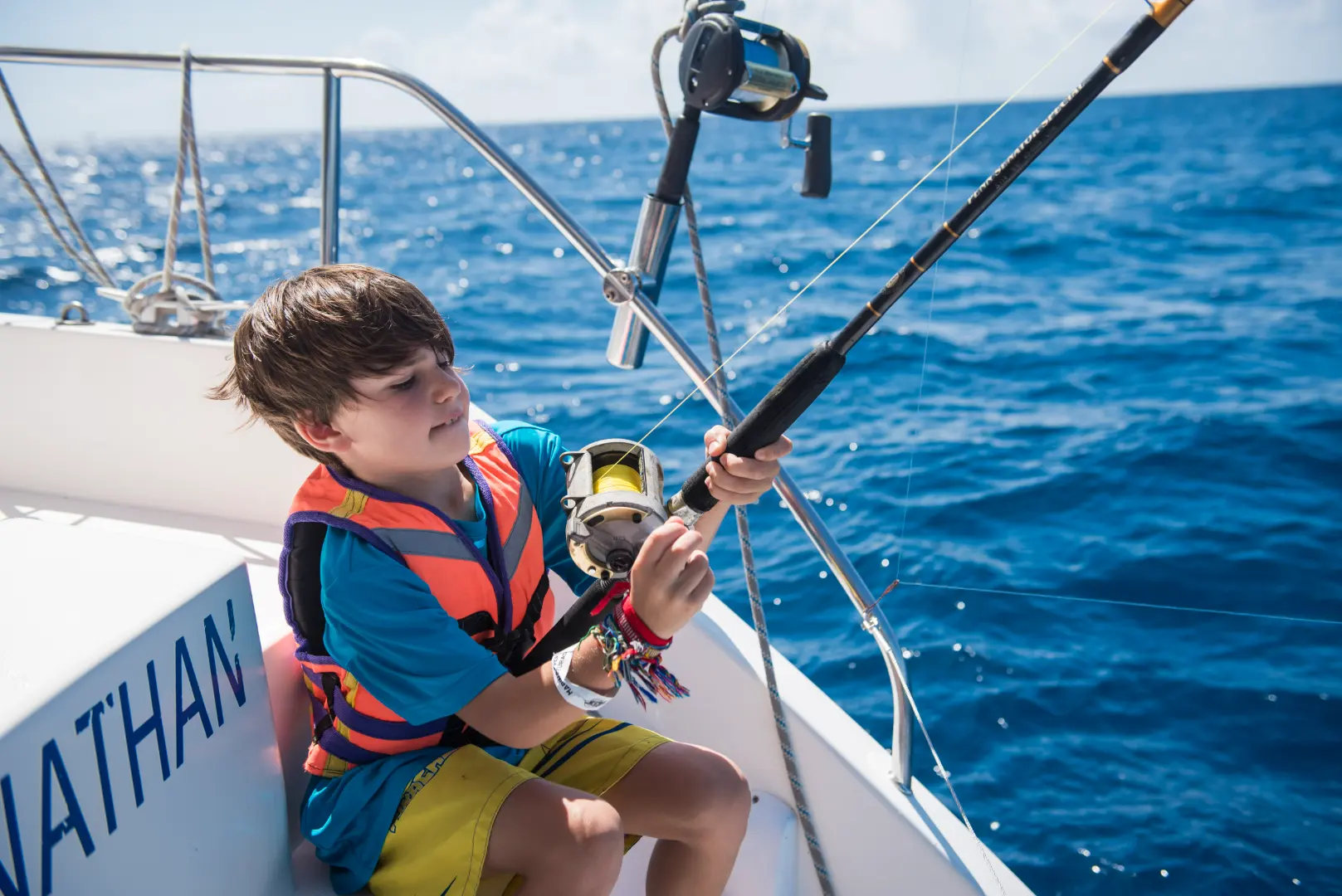 Young boy in a life vest fishing from a boat.