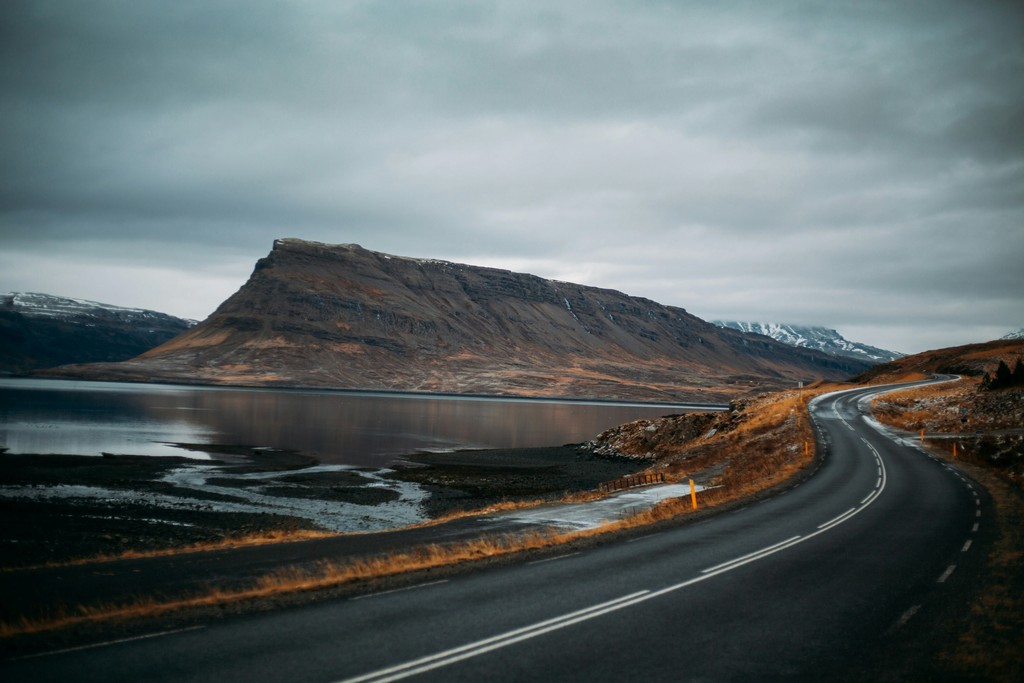 A winding road next to a lake with a mountain in the background