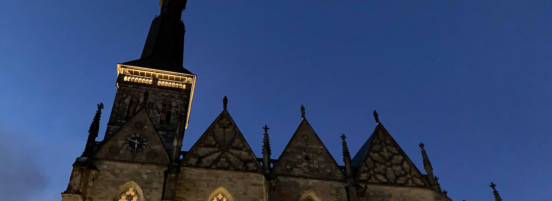 Nachtaufnahme gotischer Kirche mit hohem Turm und blauem Himmel. Historisches Gebäude in Abendstimmung.