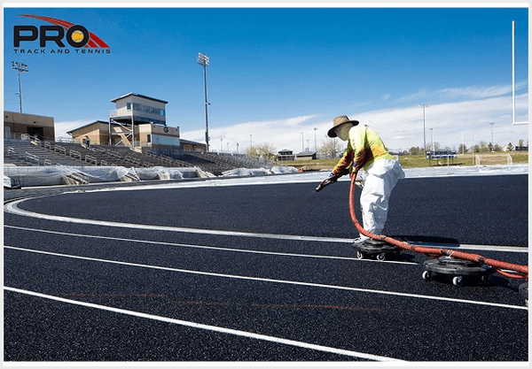 Pro Track & Tennis crew member applying surface material to a running track during installation.