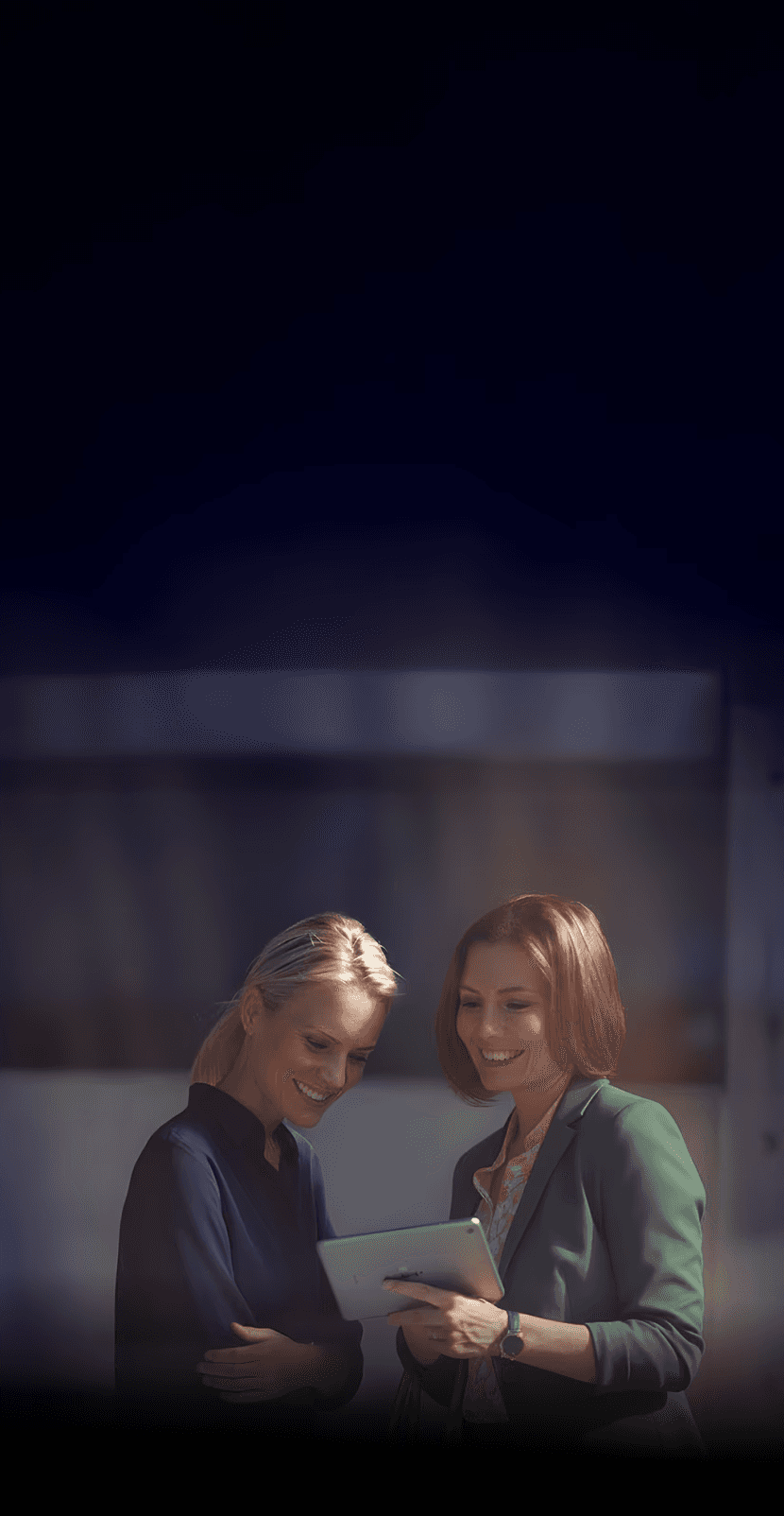 Channel partner - Two women looking at a tablet, smiling. One is wearing a green blazer and holding a yellow bag.