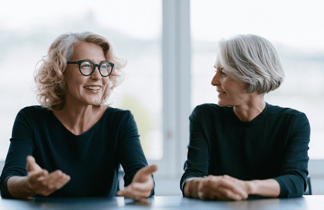 Duas mulheres maduras conversando sorrindo em um escritório bem iluminado. Blog post da Inspira sobre agentes.