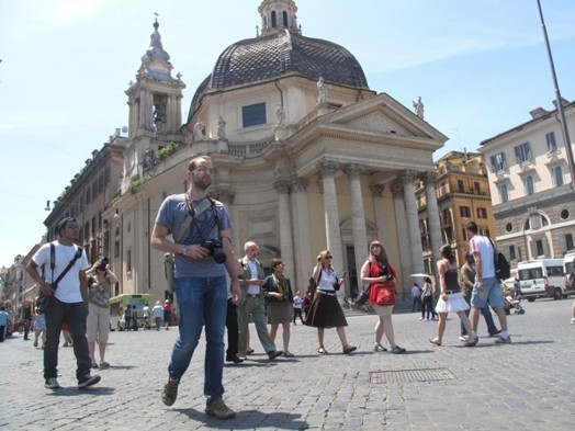 A photo of a group of people walking in an old paved square near ancient buildings.