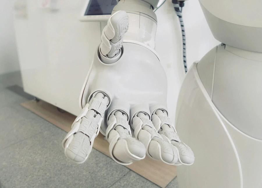 Close-up of a white humanoid robot’s hand extended forward, showing intricate mechanical joints and fingers, symbolizing artificial intelligence and robotics technology.