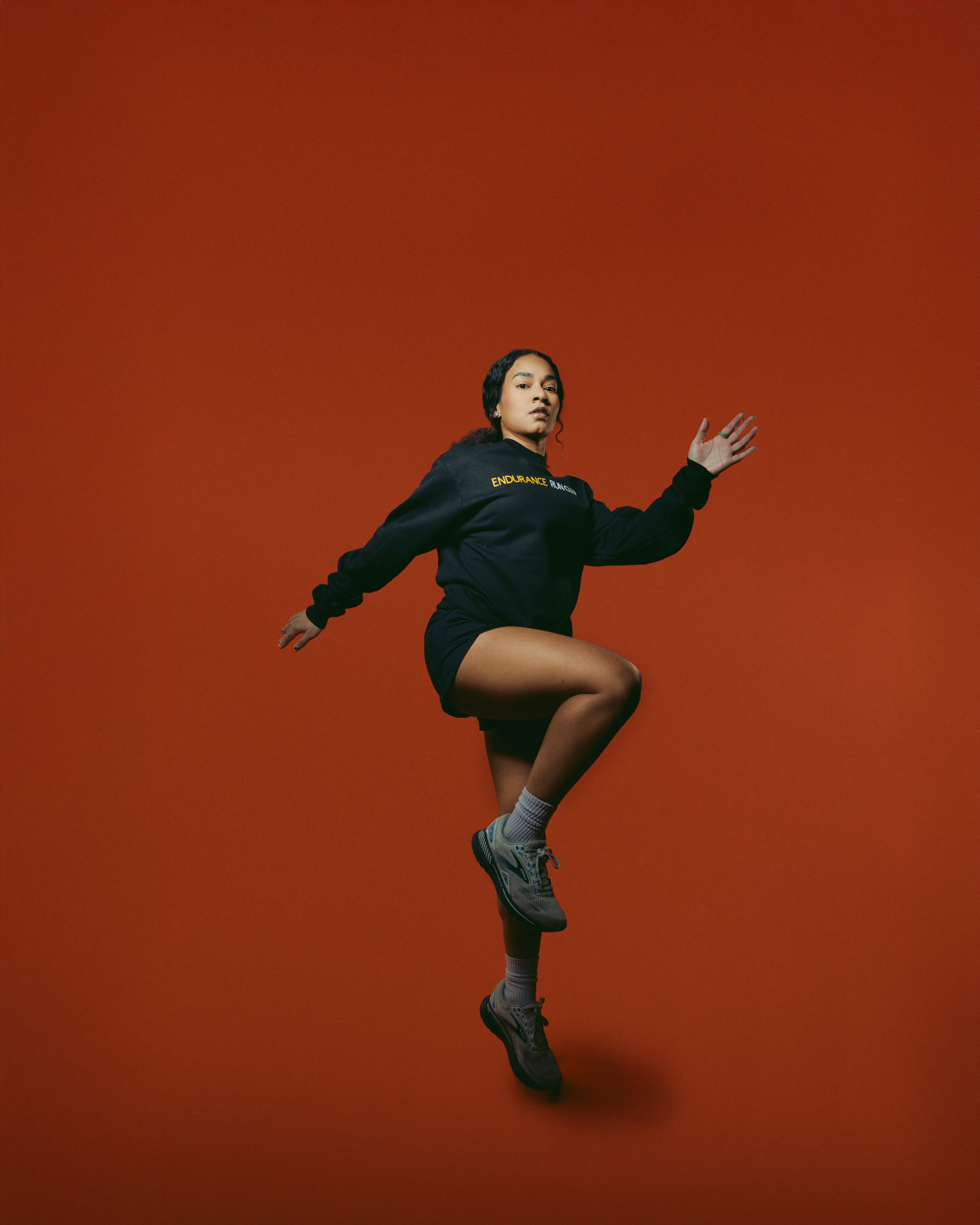 runner from endurance run club lifting one knee mid-stride against a red studio backdrop